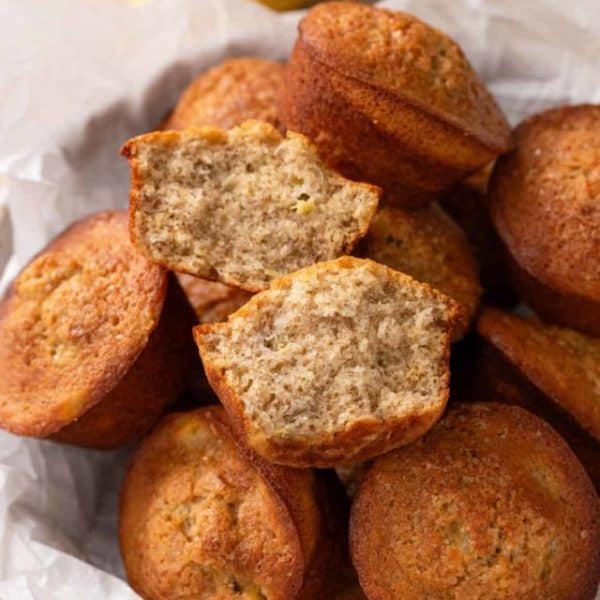 Basket of banana bread muffins with a halved muffin arranged on top.