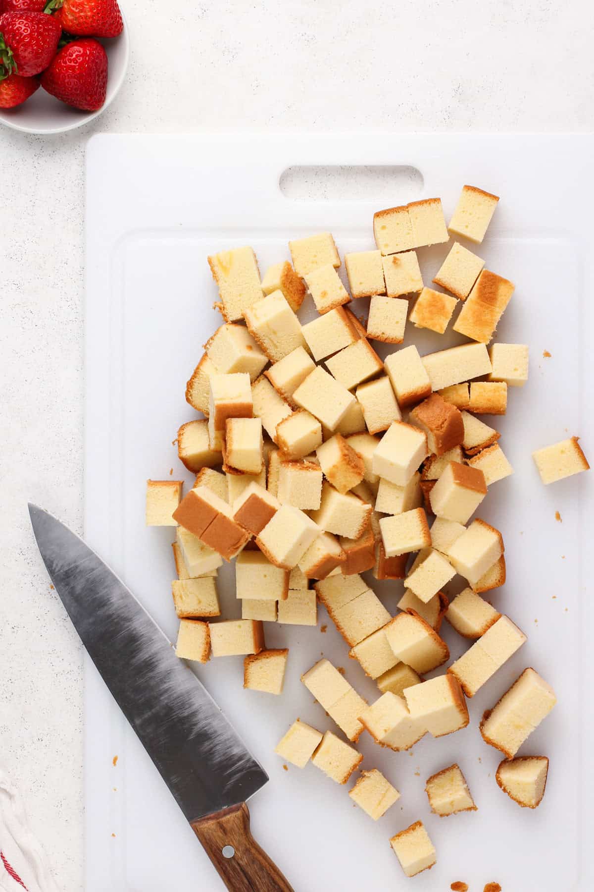 Pound cake cut into cubes on a white cutting board.