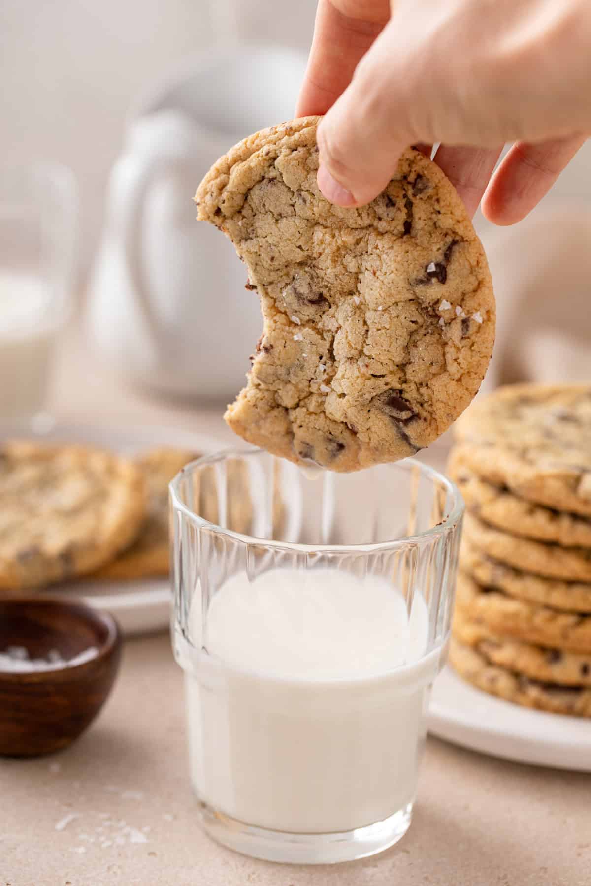 Hand about to dunk an easy chocolate chip cookie with a bite taken out of it into a glass of milk.