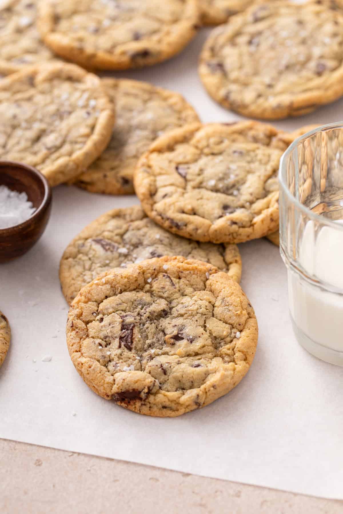 Easy chocolate chip cookies scattered on a piece of parchment paper next to a glass of  milk.