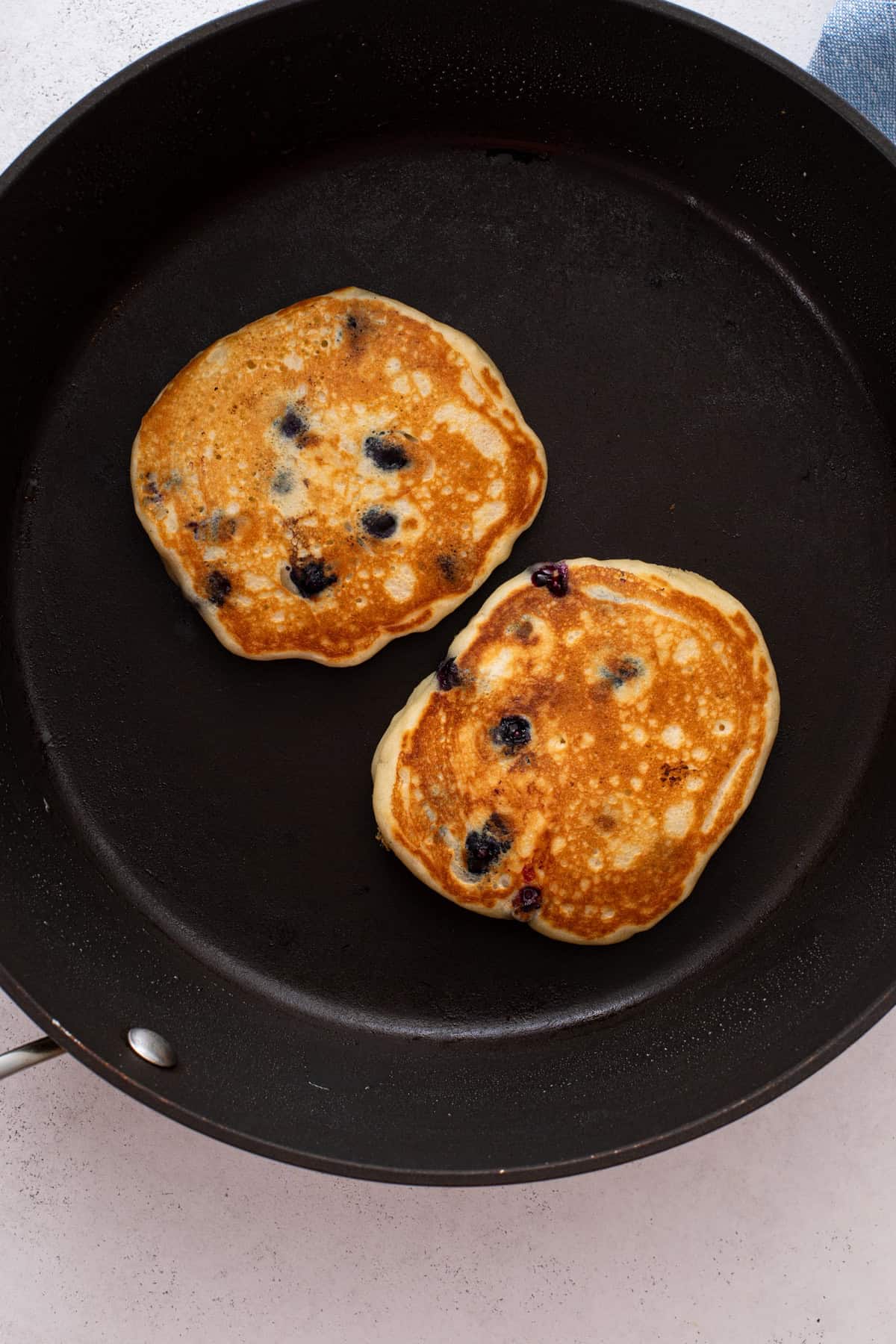 Two flipped blueberry pancakes in a black skillet.