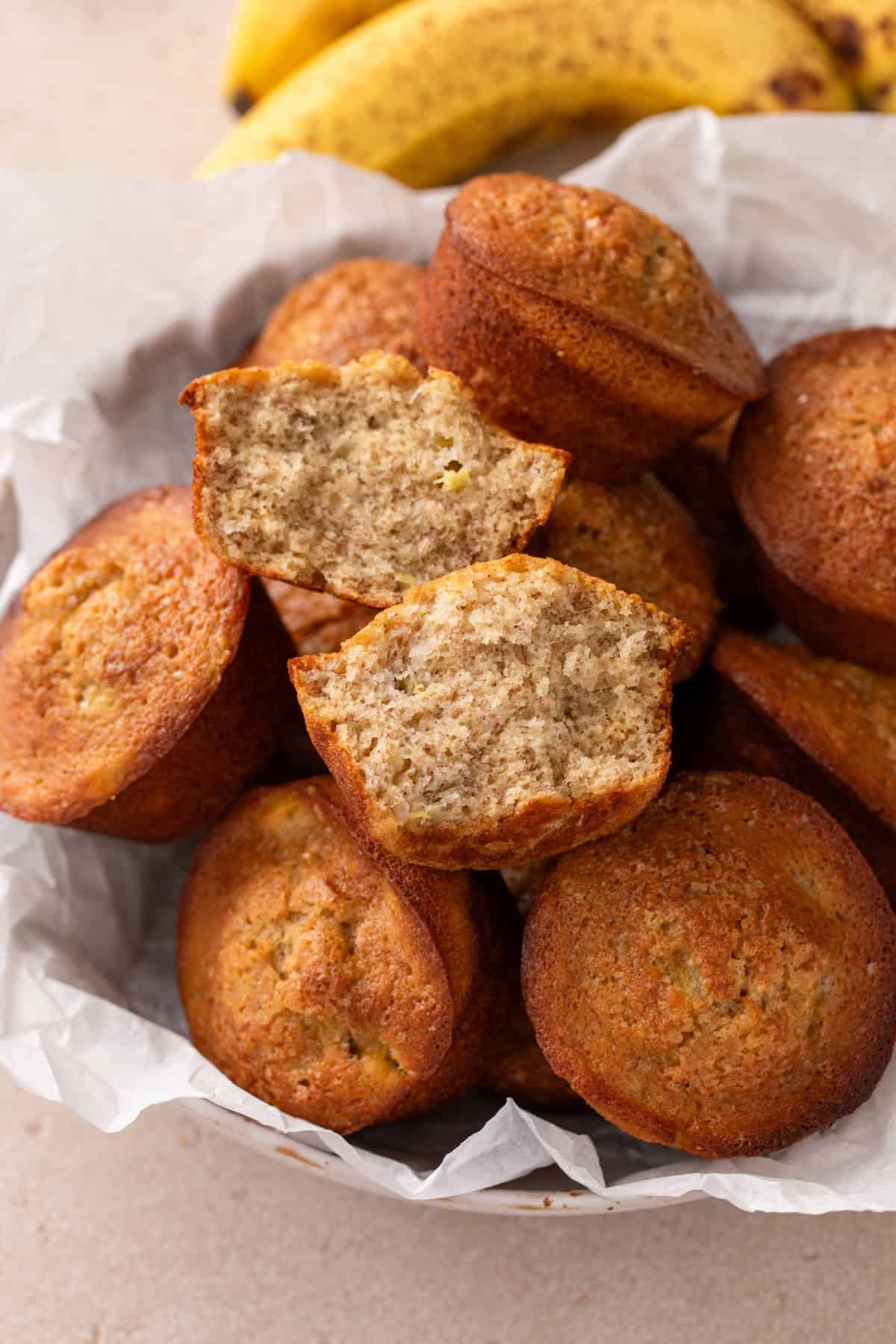 Basket of banana bread muffins with a halved muffin arranged on top.