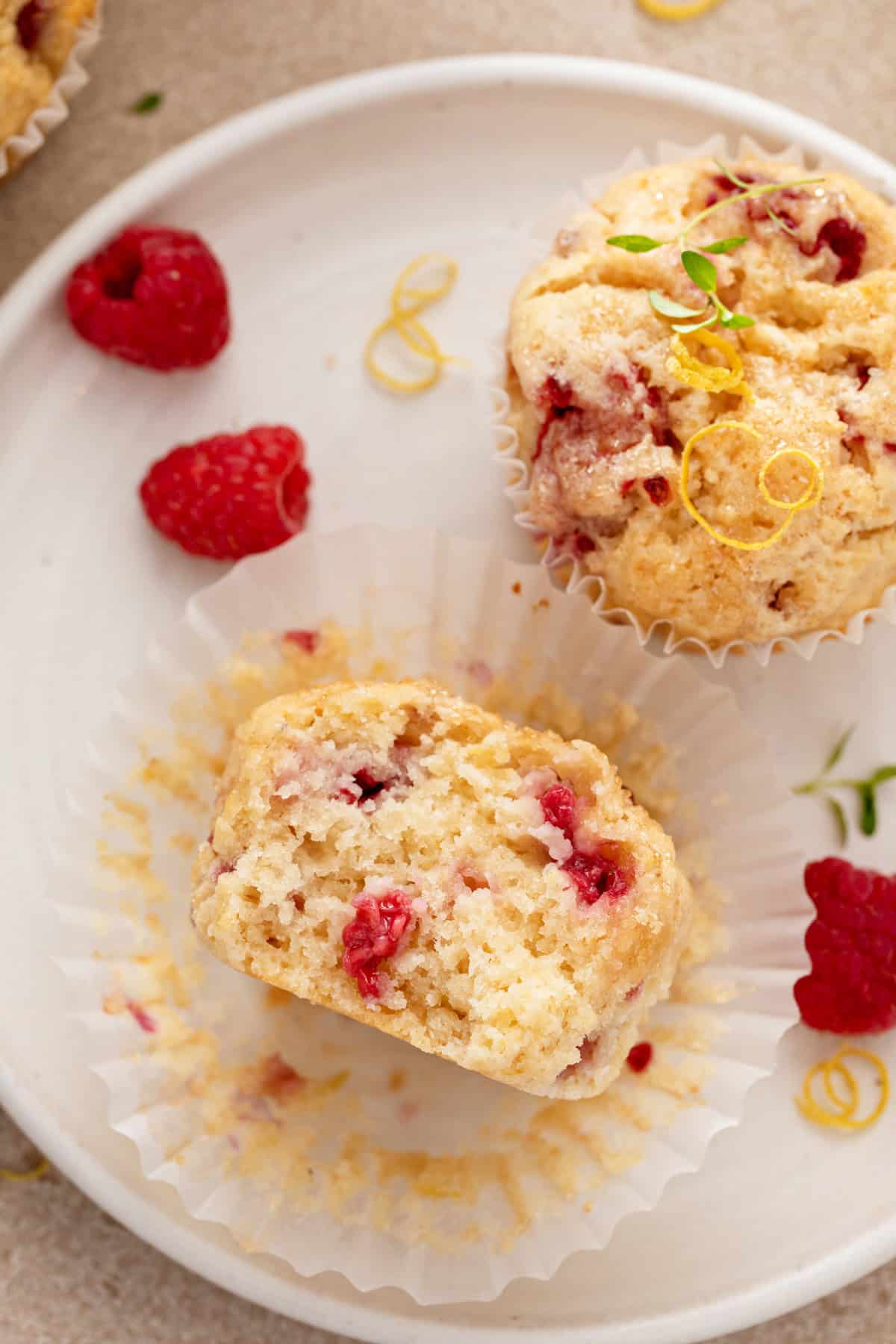 Half of a lemon raspberry muffin on a white plate next to a whole muffin.