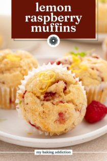 Three lemon raspberry muffins on a white plate. The muffin in front in lying on its side. Text overlay includes recipe name.