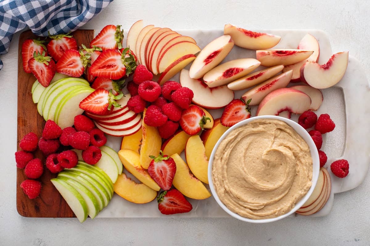 Overhead view of a bowl of peanut butter dip on a platter of assorted fresh fruit.