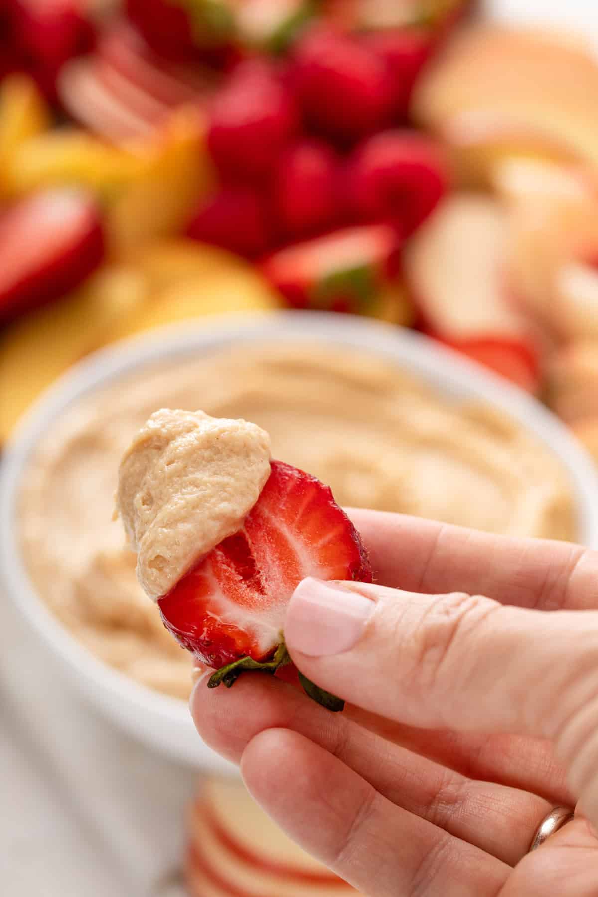 Hand holding up half a strawberry dipped in peanut butter dip.