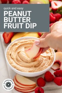 Hand dipping a slice of white peach into a bowl of peanut butter dip. Text overlay includes recipe name.