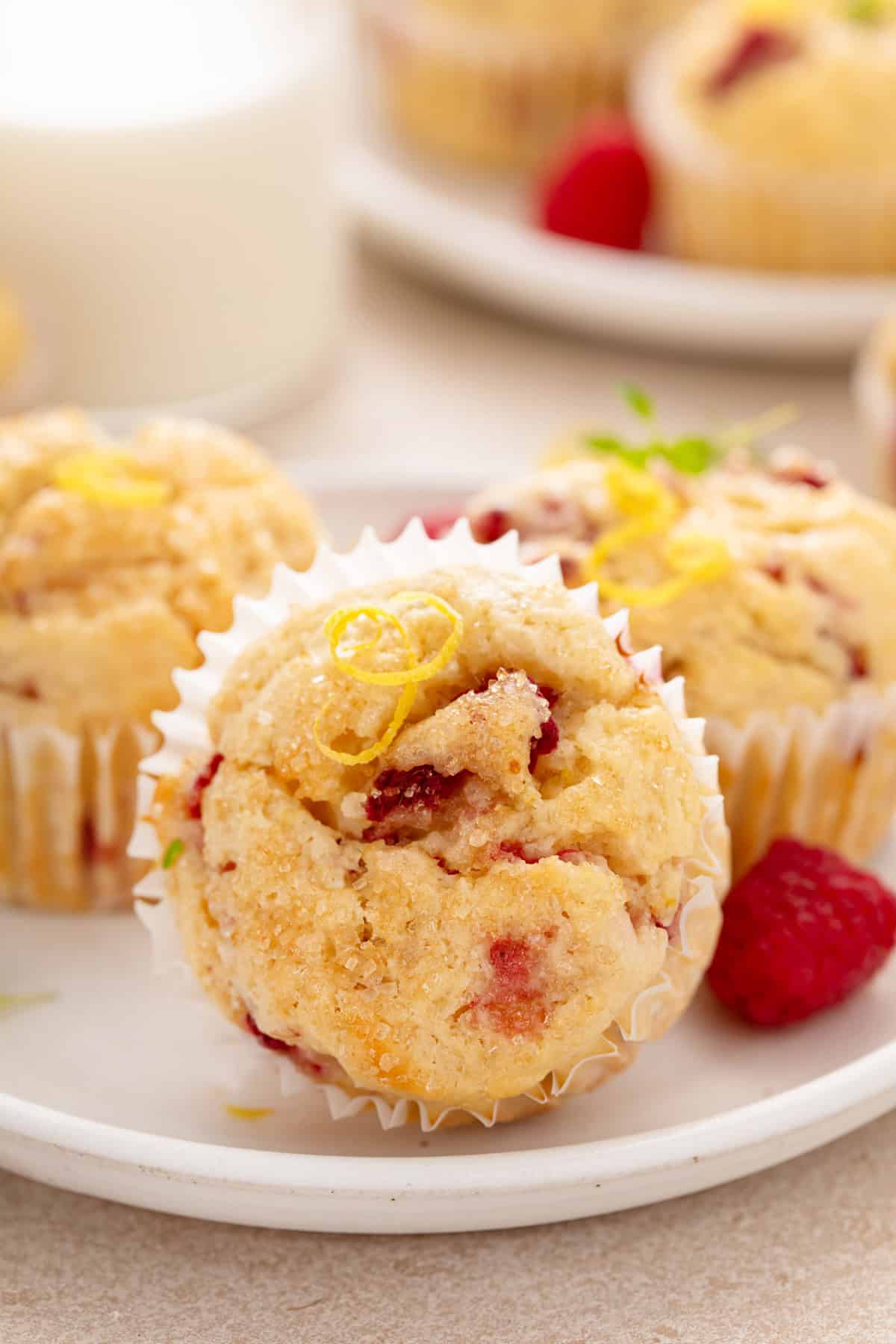 Three lemon raspberry muffins on a white plate. The muffin in front in lying on its side.