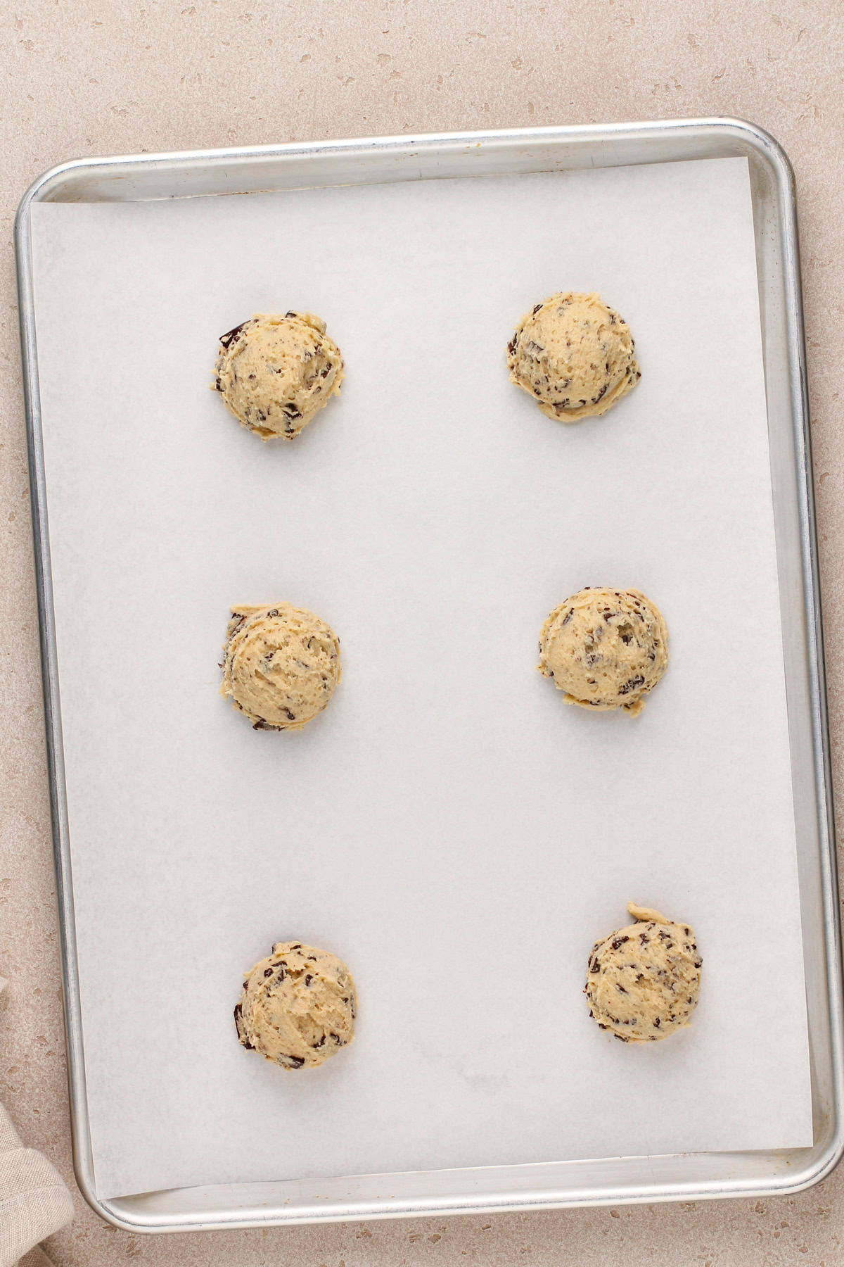 Scoops of easy chocolate chip cookie dough on a lined baking sheet.