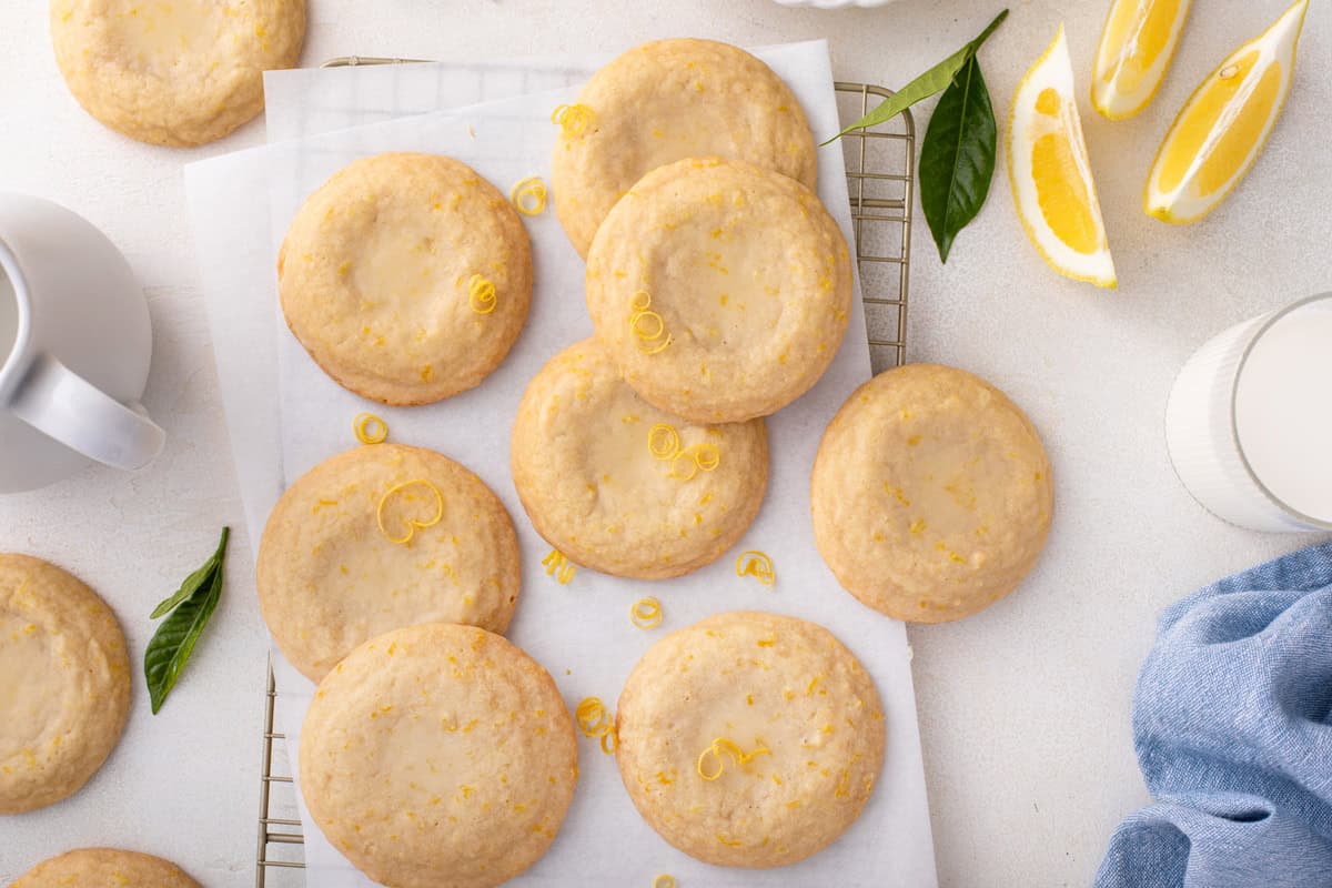 Overhead view of several glazed lemon cookies scattered on a piece of parchment paper over a wire rack.