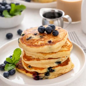 Stack of blueberry pancakes on a white plate.
