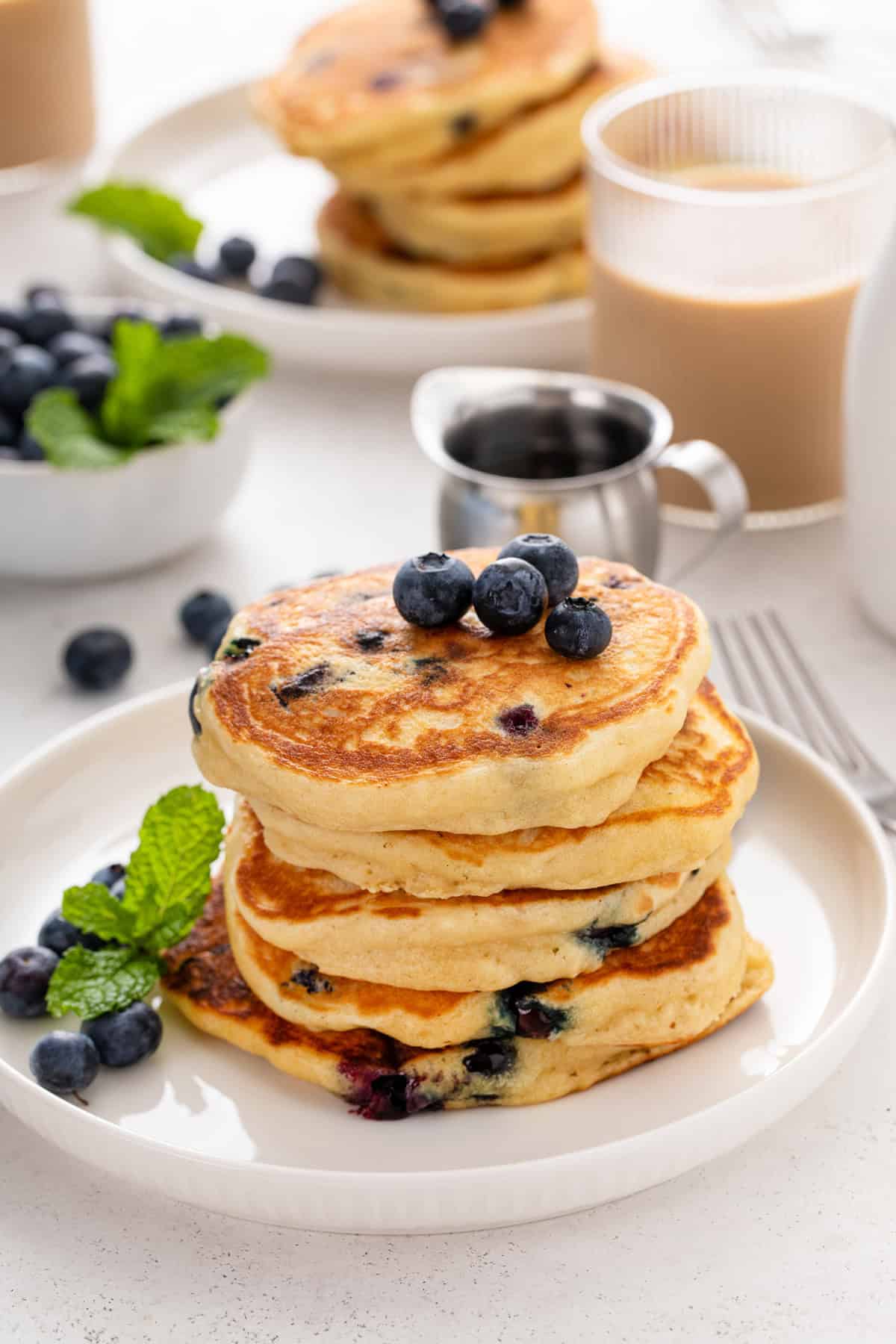 Blueberry pancakes stacked on a white plate and topped with fresh blueberries.