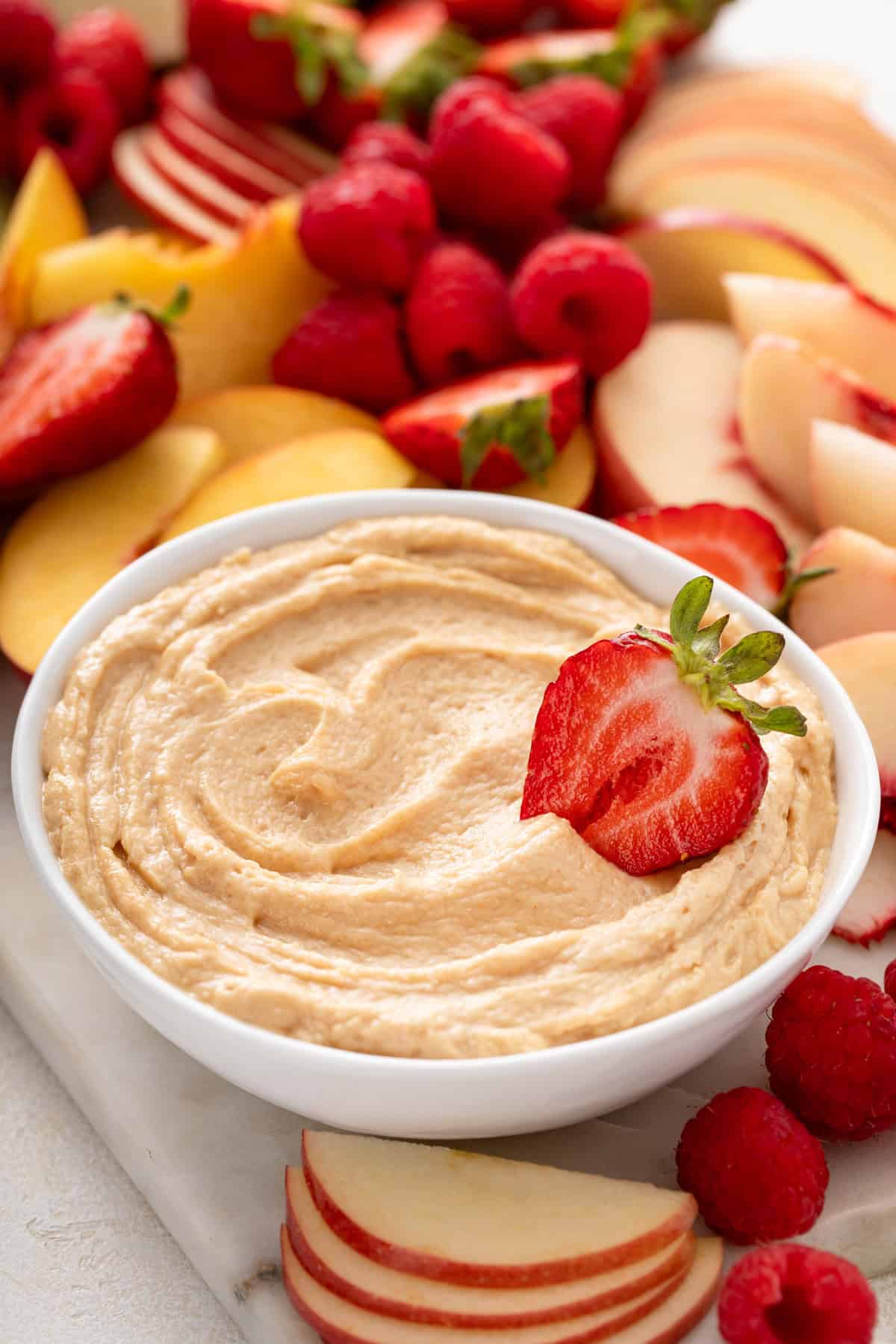 White bowl of peanut butter dip with half a strawberry in it.