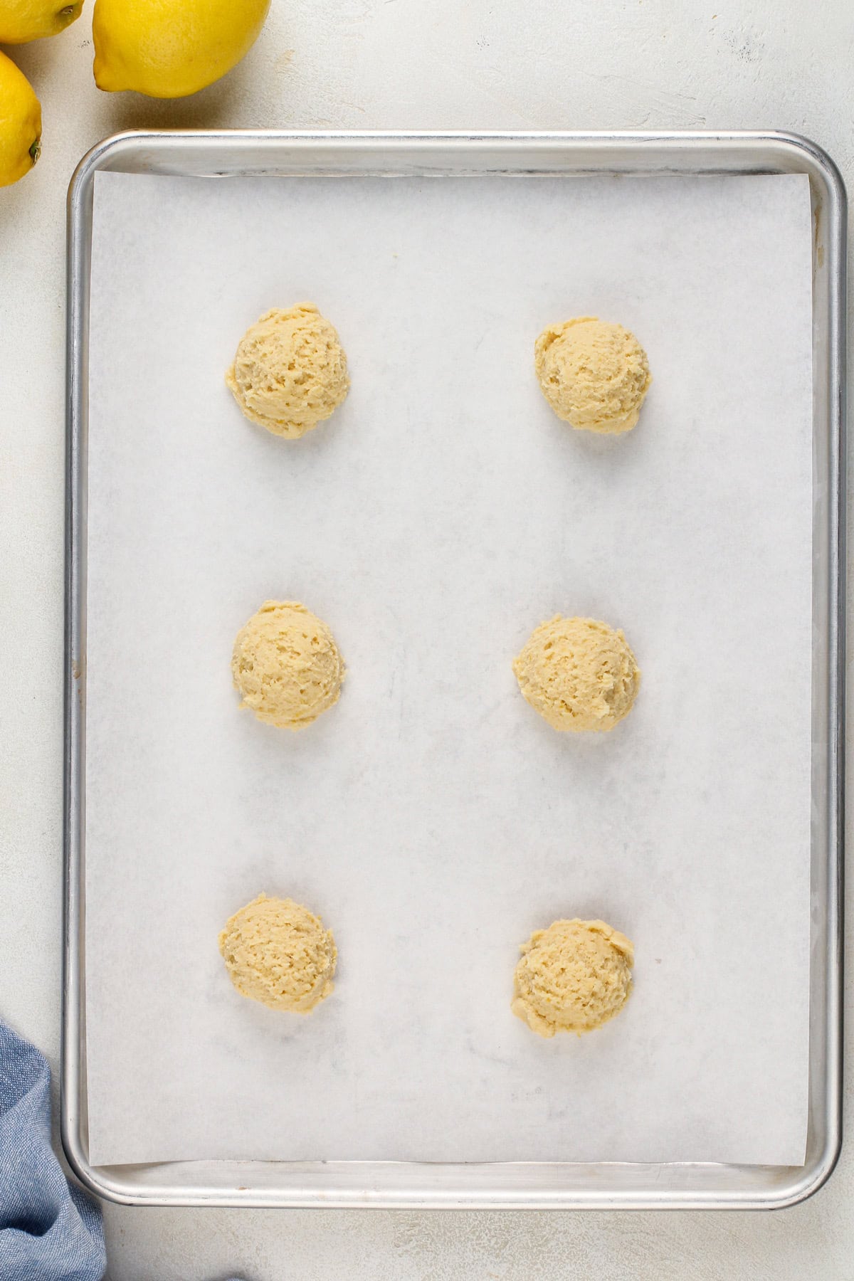 Lemon cookie dough balls on a parchment-lined baking sheet, ready to go in the oven.