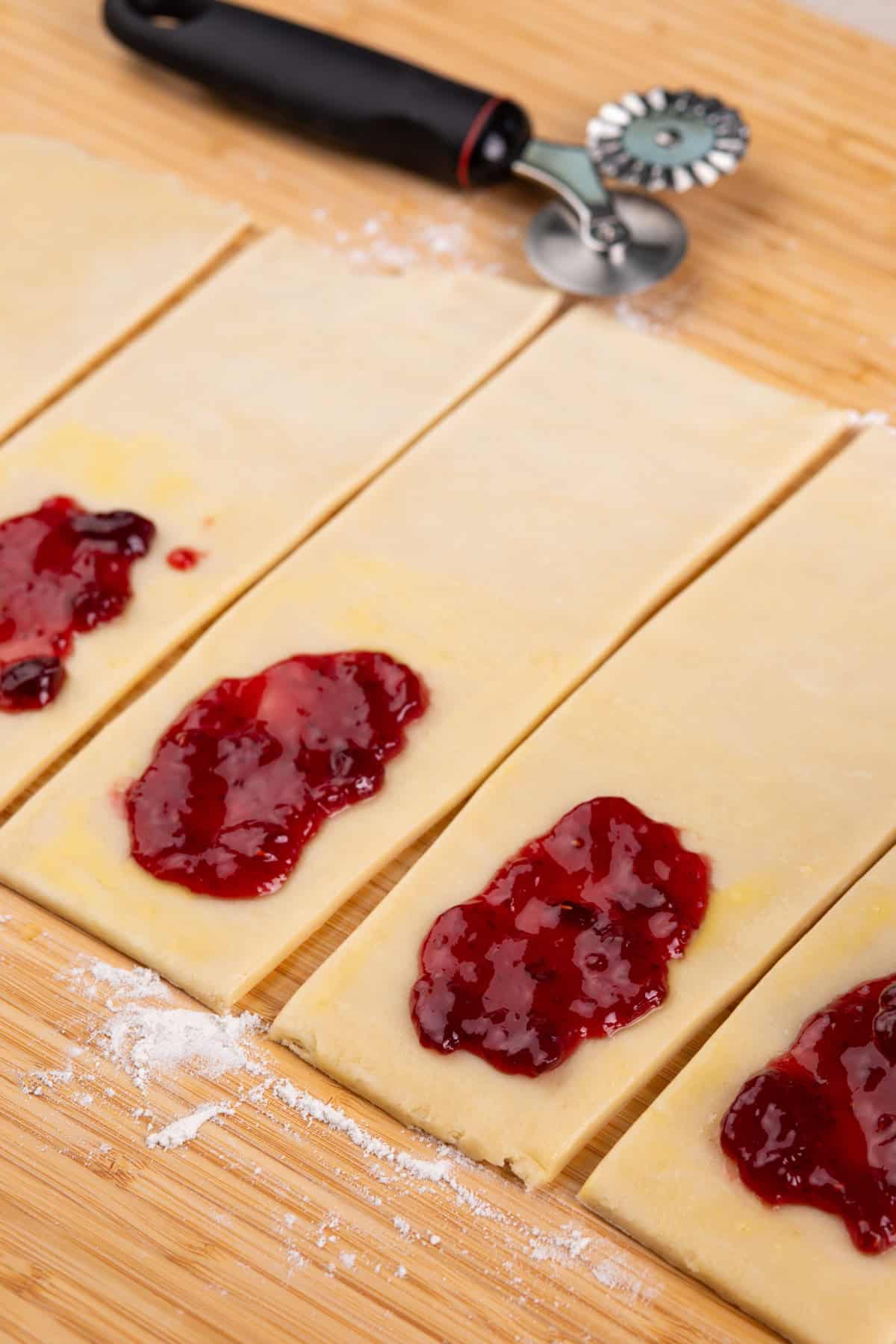 Raspberry jam spread on half of pie dough rectangles.