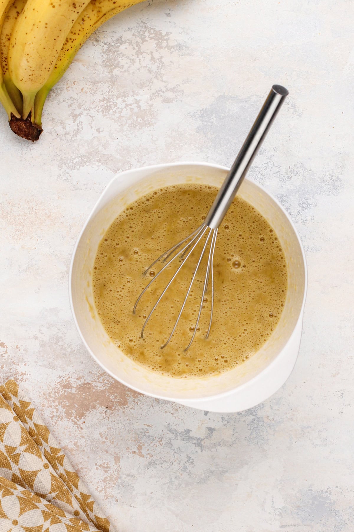 Wet ingredients for pineapple banana bread whisked together in a white bowl.