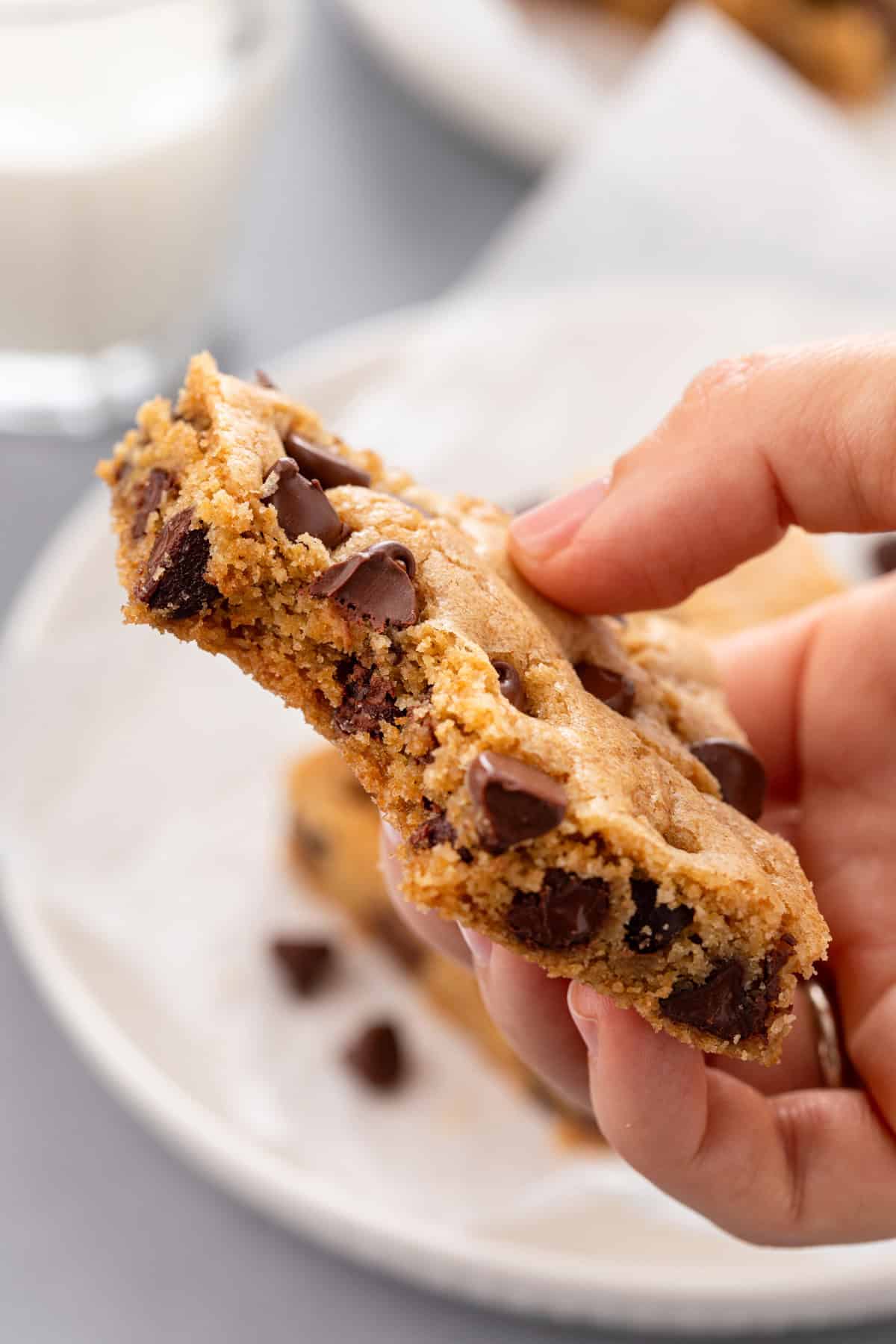 Hand holding up a chocolate chip cookie bar with a bite taken from it.