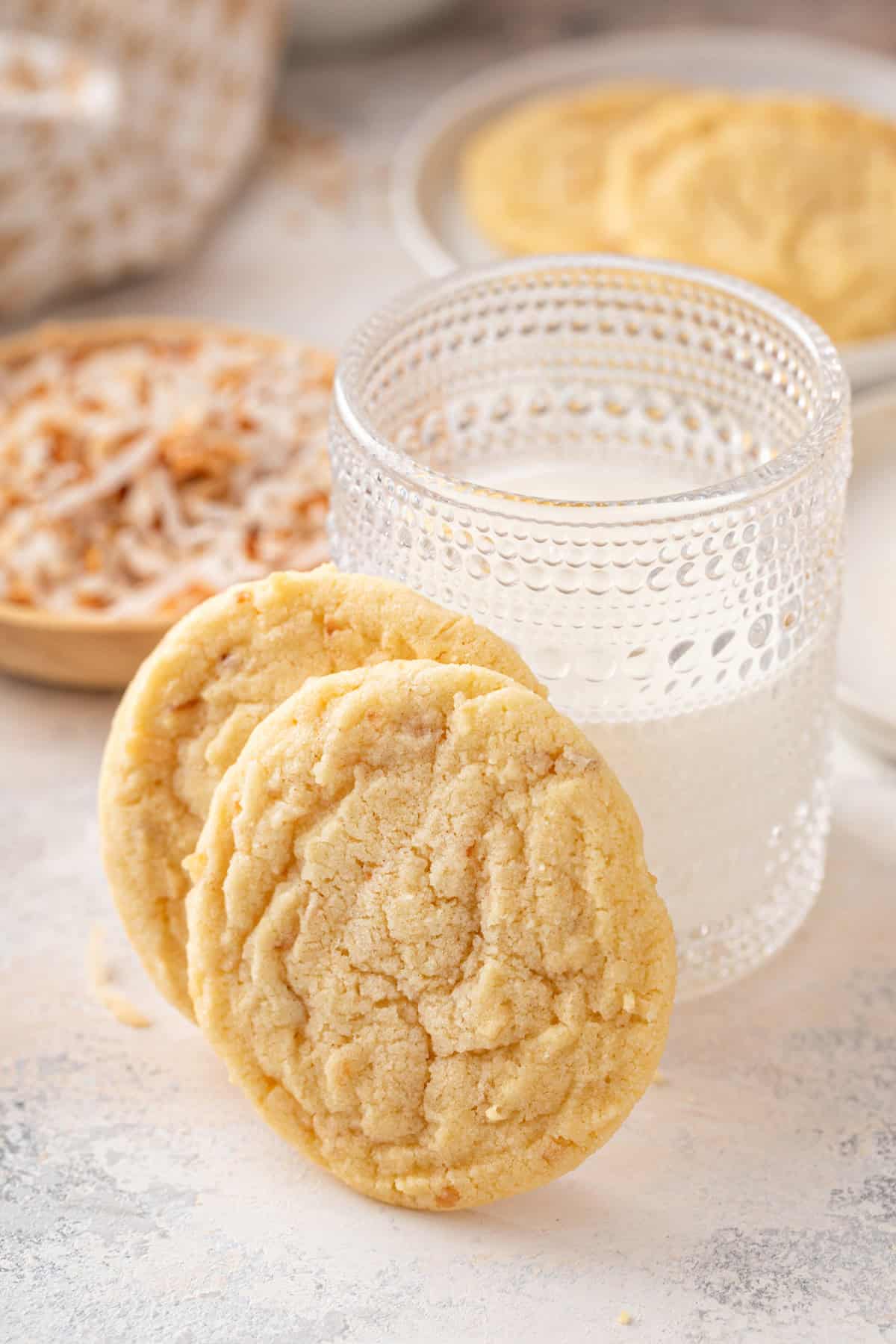 Two coconut sugar cookies leaning against a glass of milk.