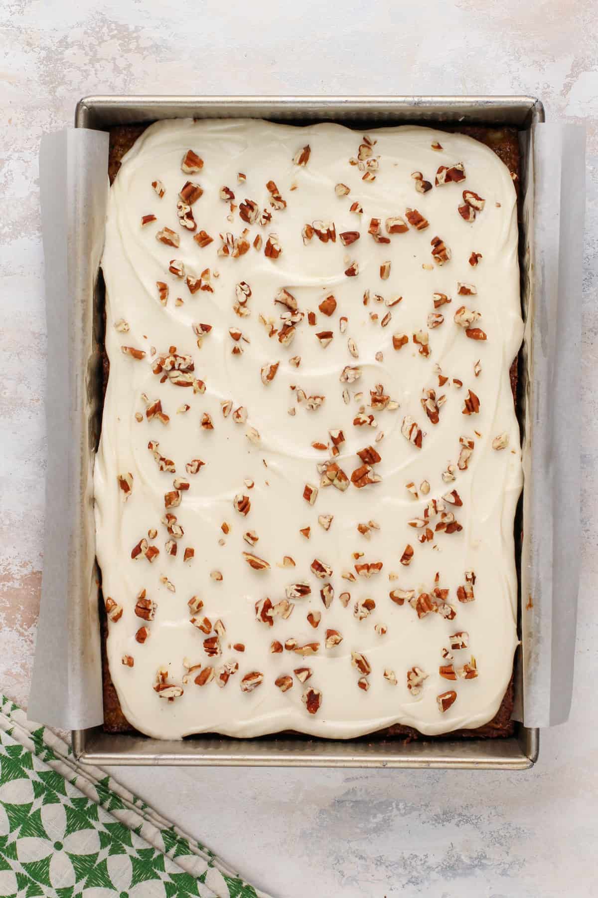 Cream cheese frosting spread over pineapple zucchini cake, topped with chopped pecans.