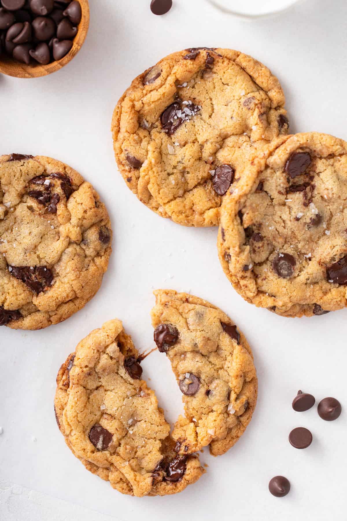 Several heath bar cookies on a countertop. One cookie is cut in half to show the gooey chocolate chips.