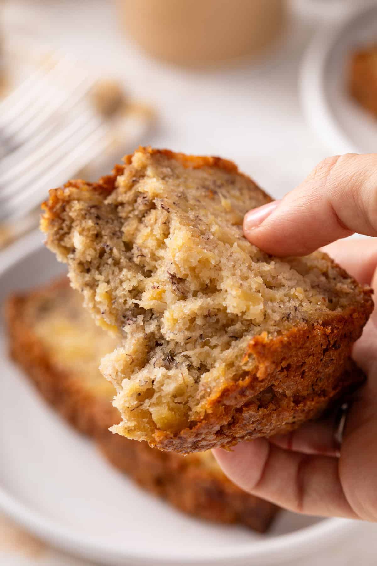 Hand holding up a slice of pineapple banana bread broken in half.