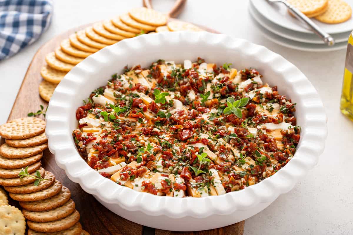 White deep dish pie plate filled with marinated cheese on a board with crackers.