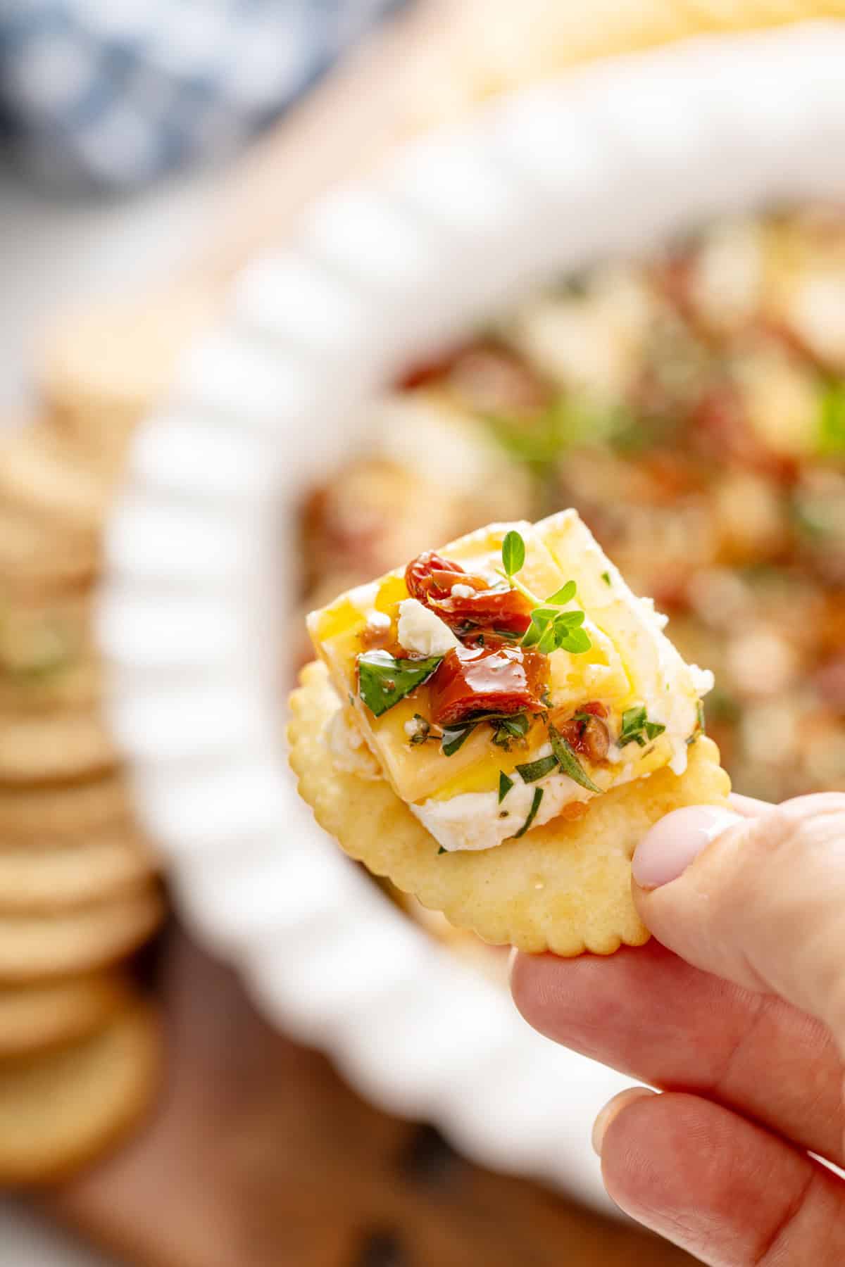 Hand holding up marinated cheese on a cracker.