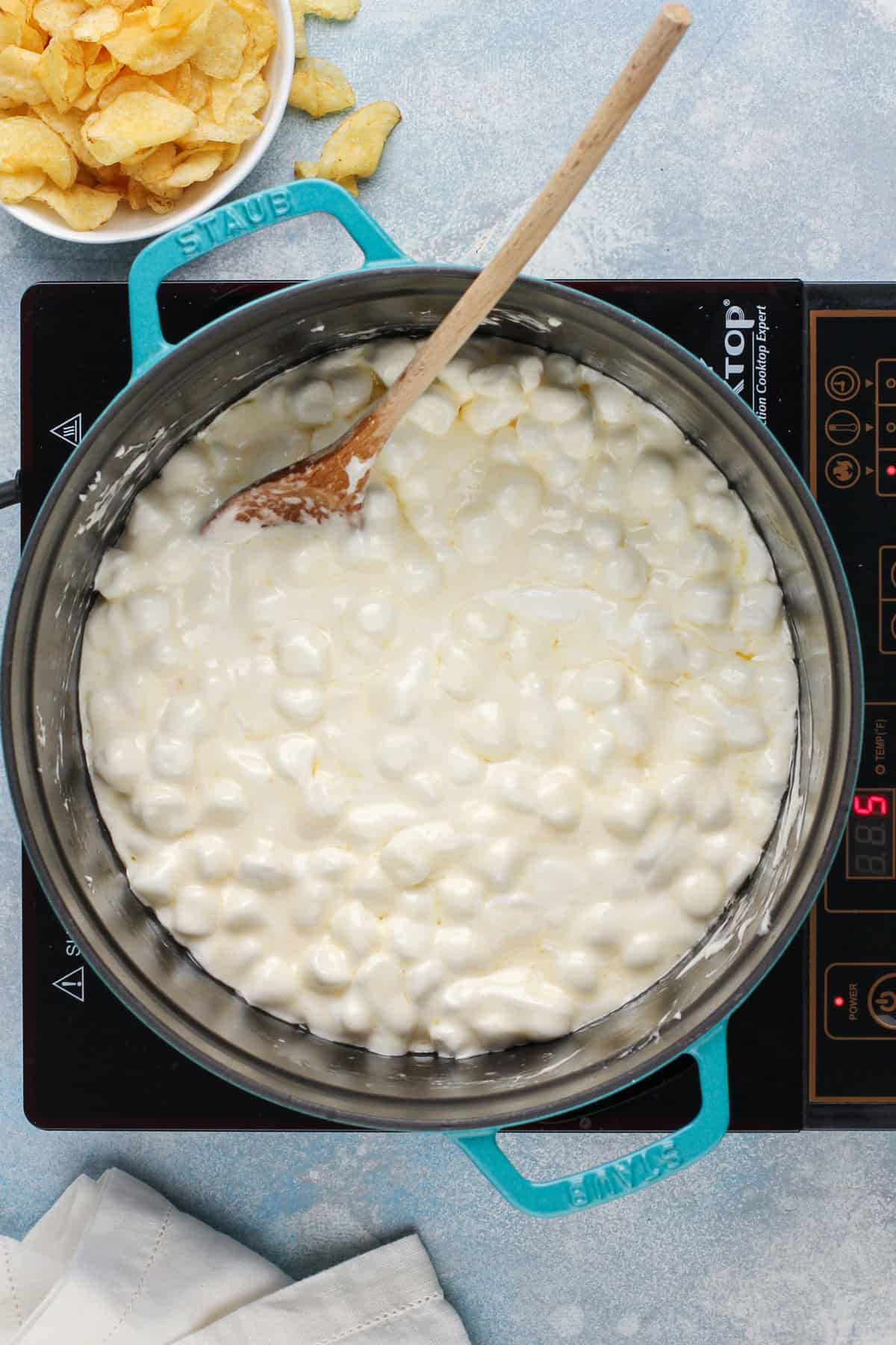 Marshmallows melting in a blue dutch oven on a stove burner.