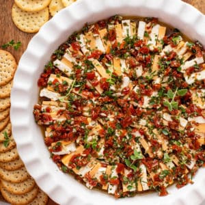 Dish of marinated cheese next to crackers.