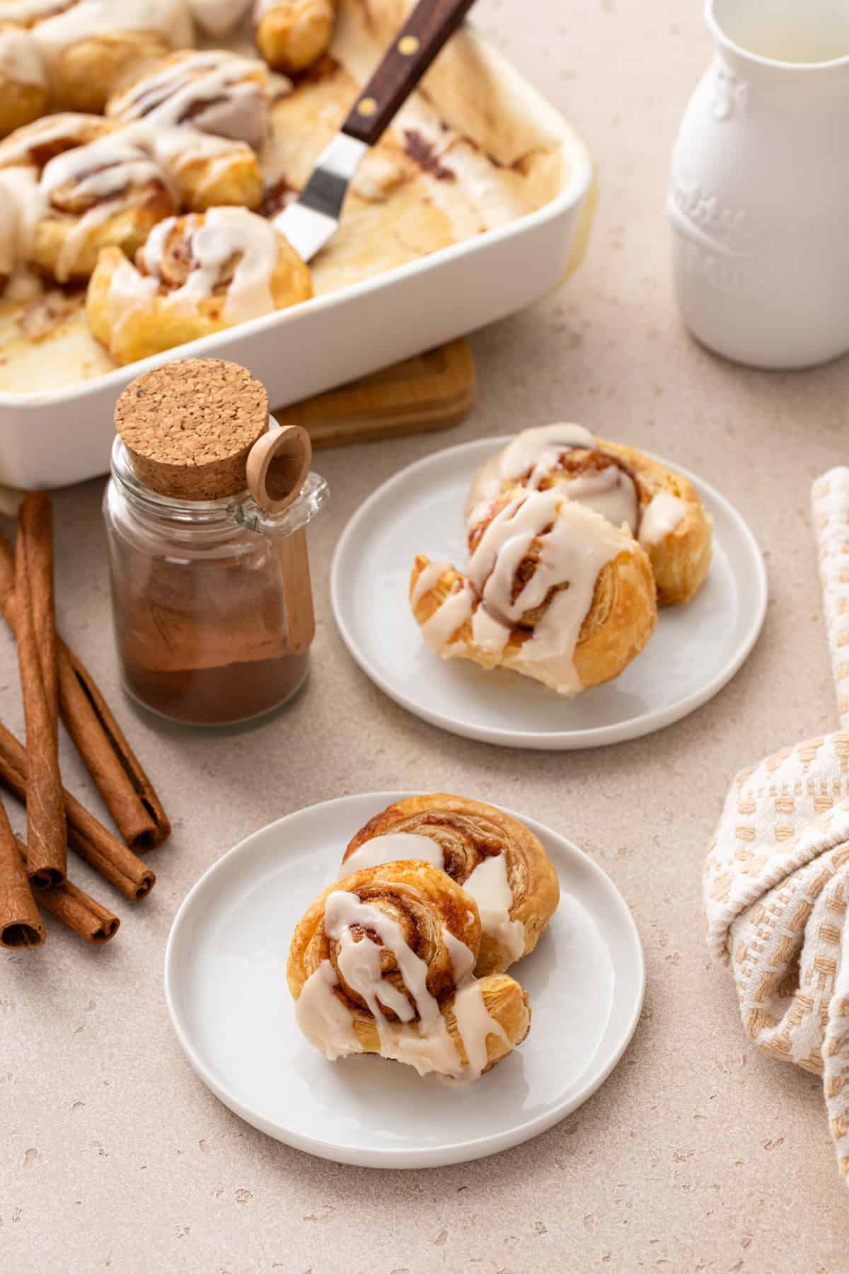 Two white plates of puff pastry cinnamon rolls on a countertop.