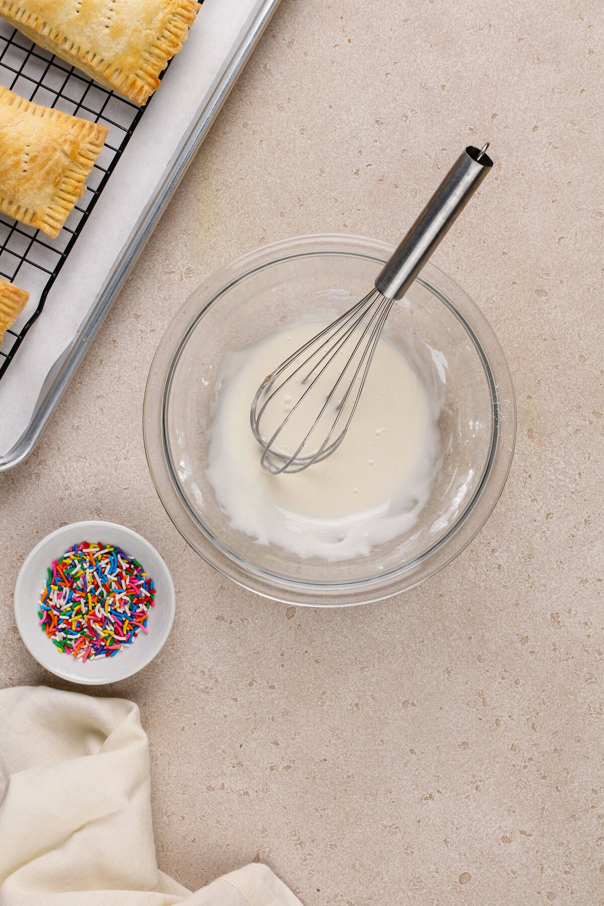 Glaze for homemade pop tarts next to a small bowl of rainbow sprinkles.