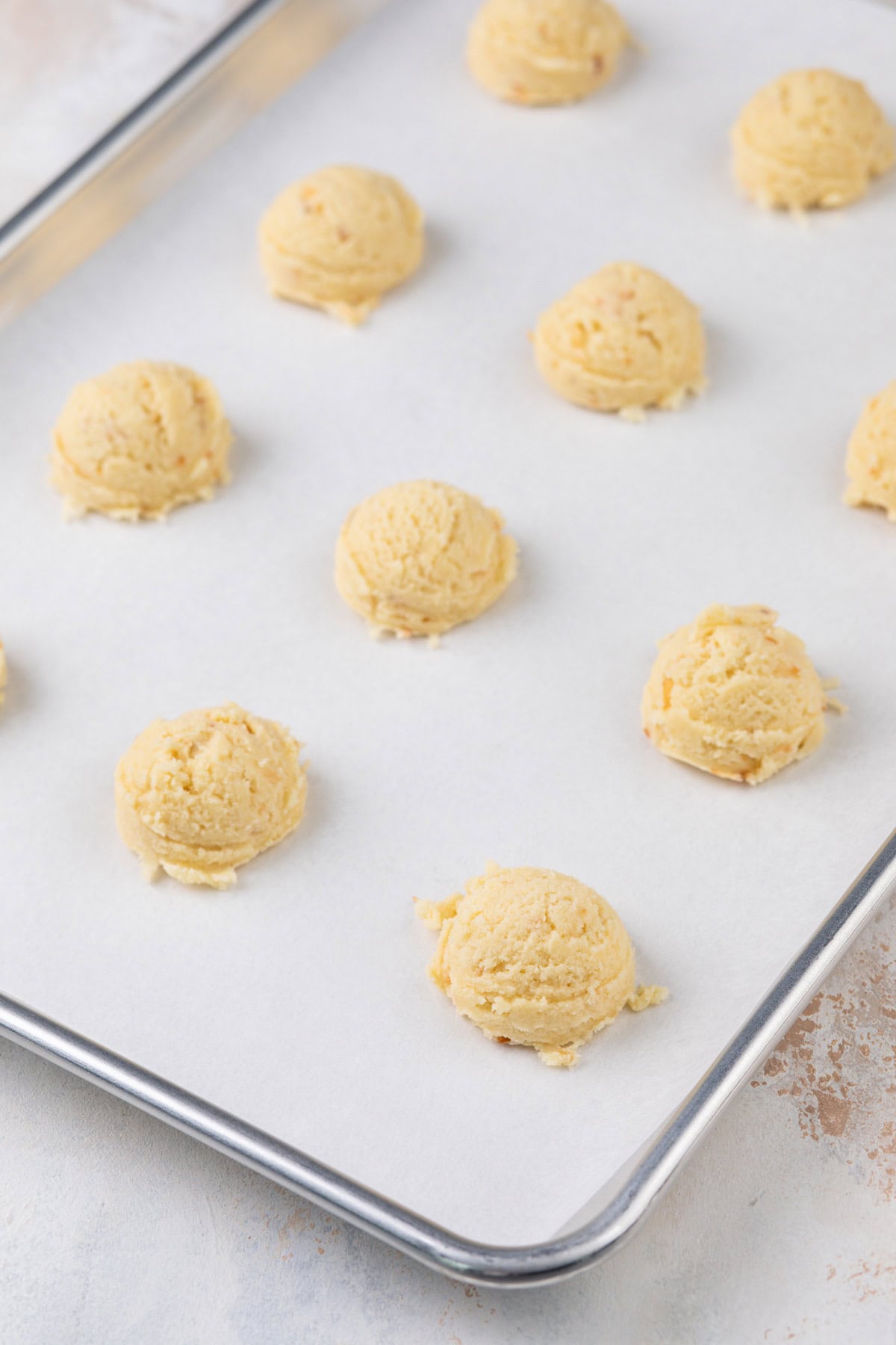 Balls of coconut sugar cookie dough on a parchment-lined baking sheet.