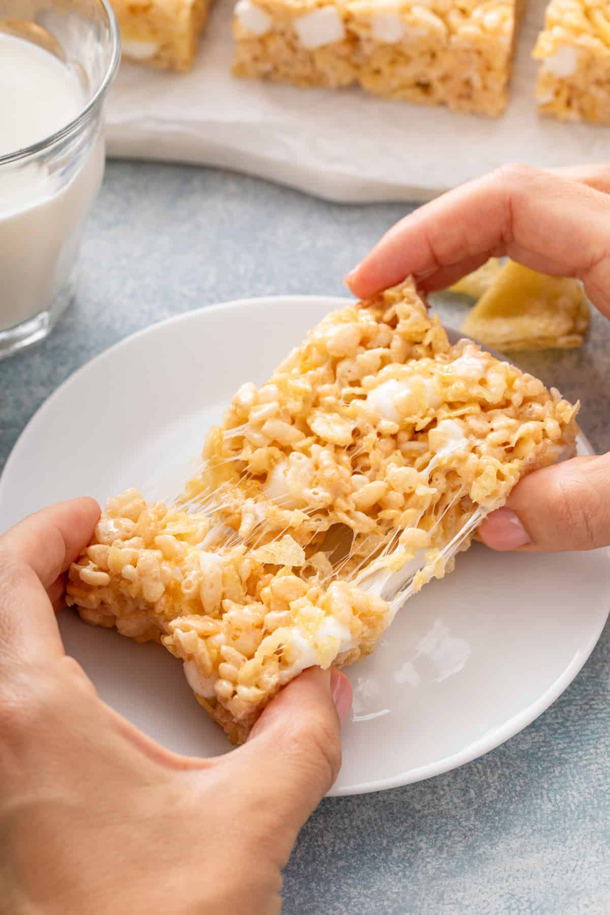 Hand pulling apart a potato chip rice krispie treat over a white plate.