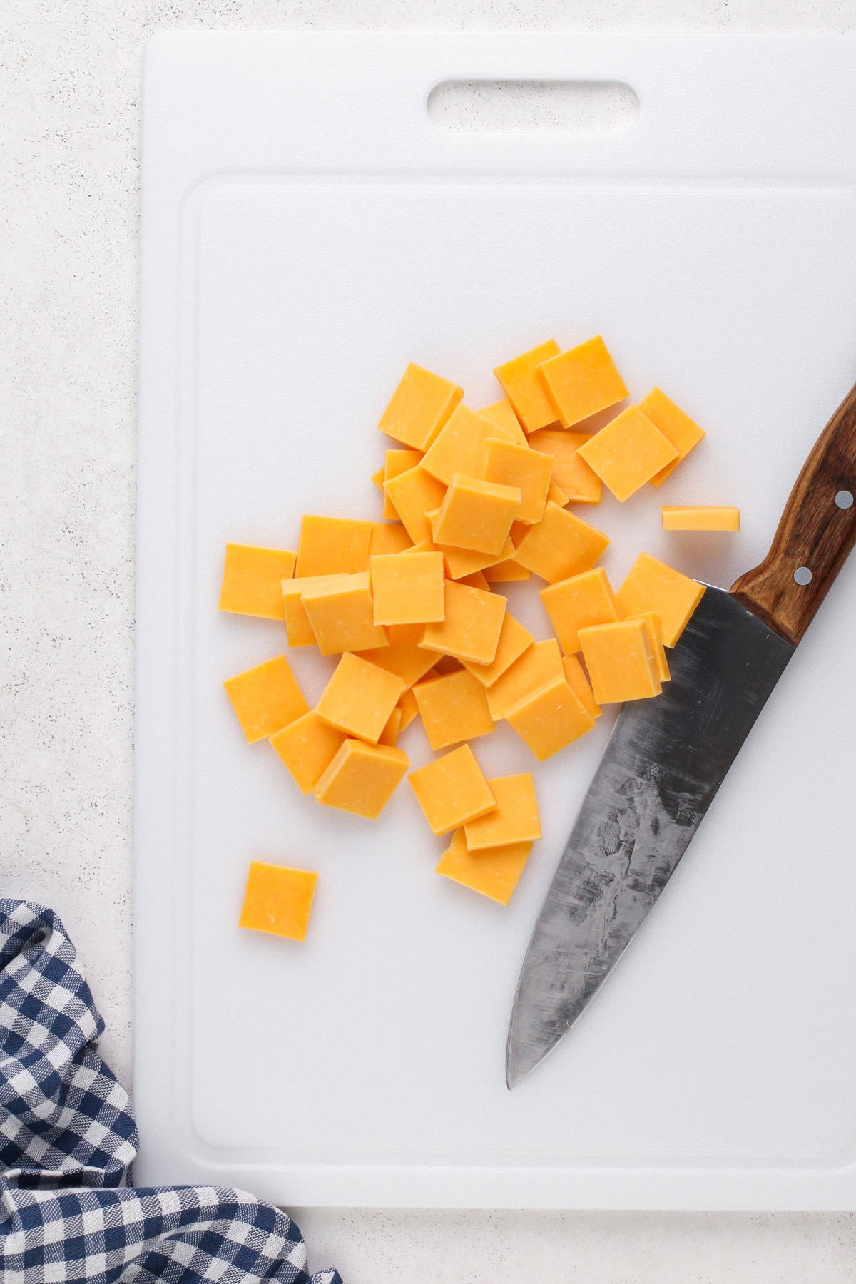 Cheddar cheese cut into squares on a white cutting board.