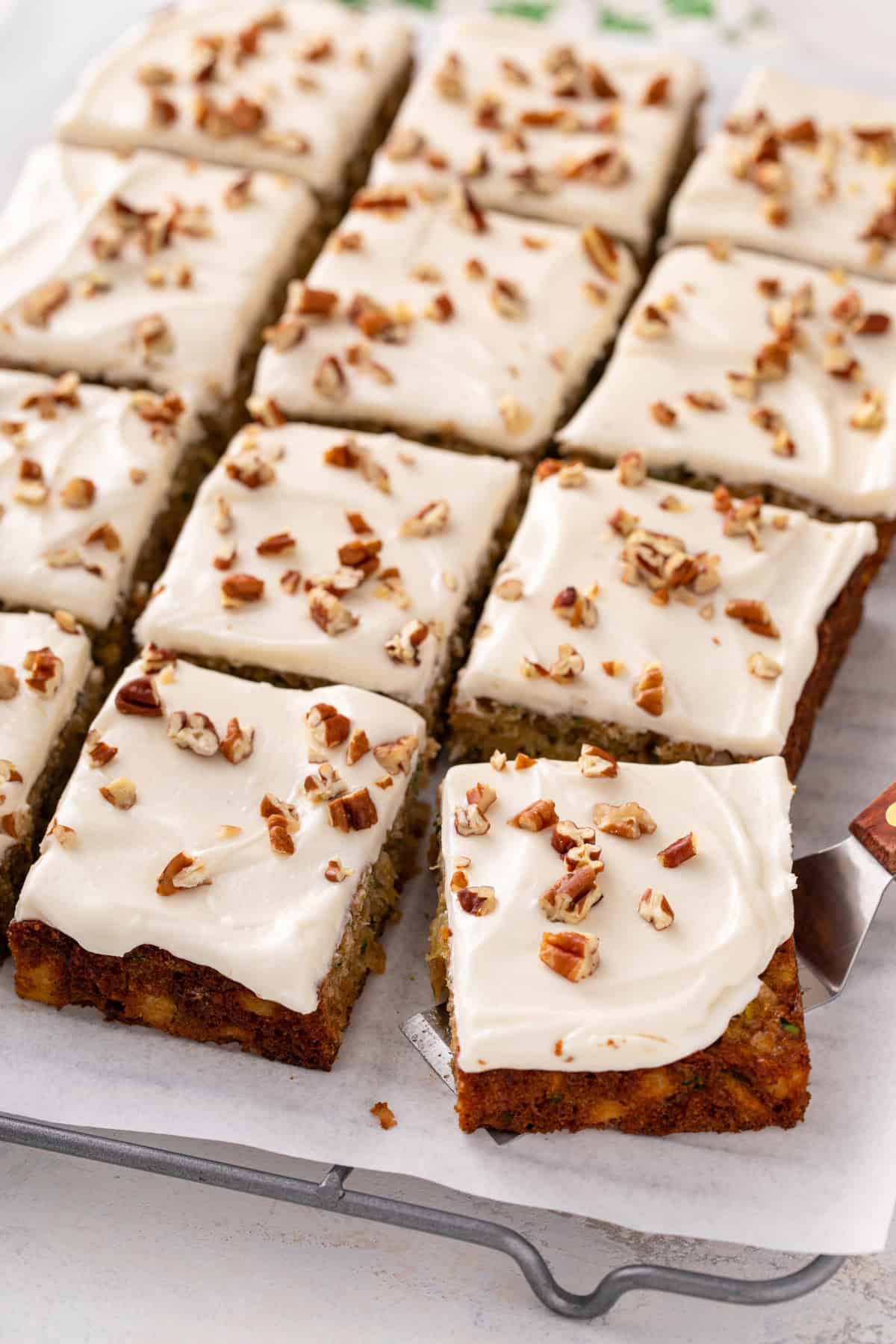 Sliced pineapple zucchini cake topped with cream cheese frosting and pecans.