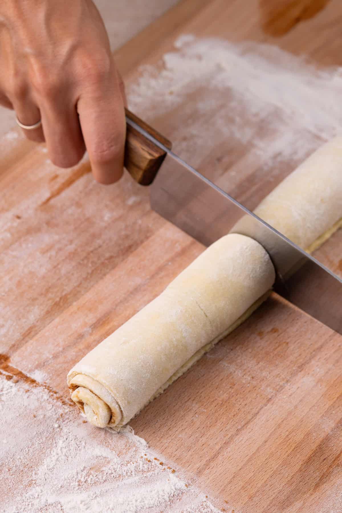 Knife cutting a roll of puff pastry cinnamon rolls.