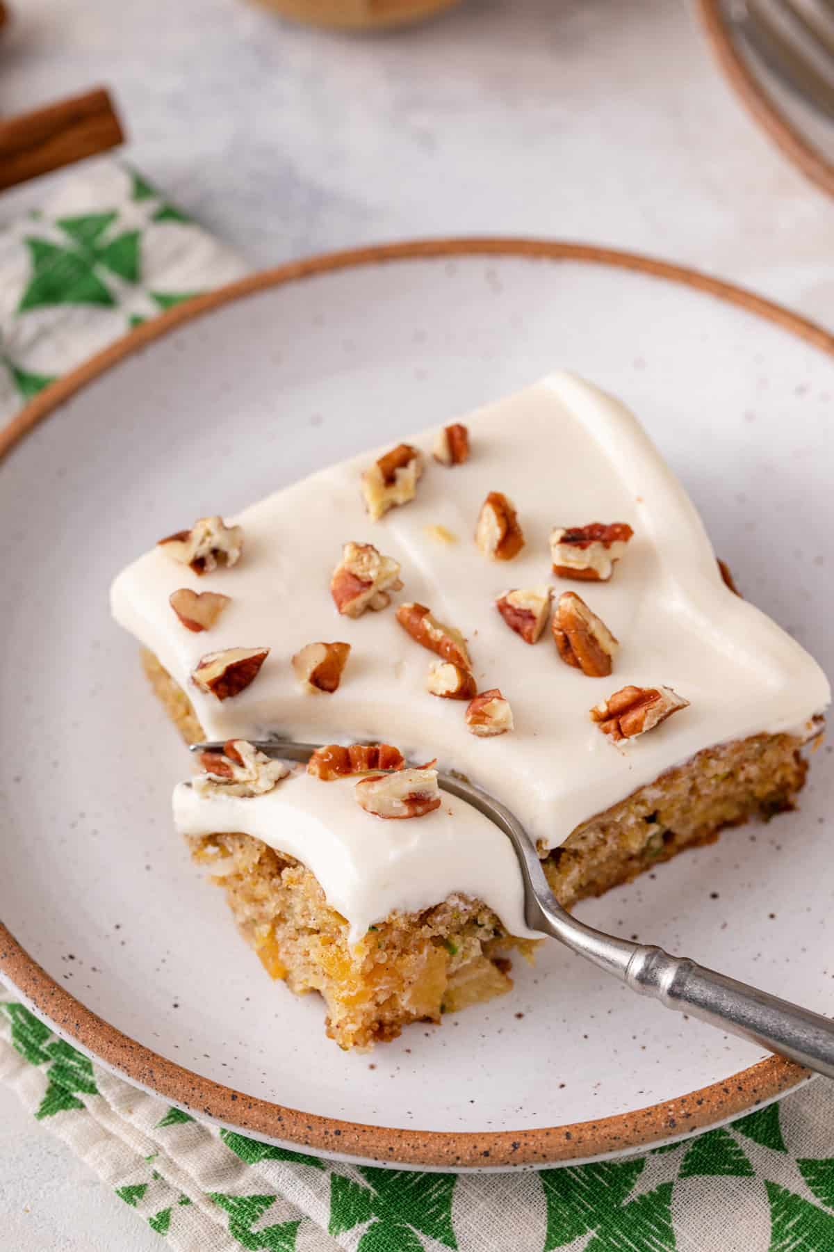 Fork cutting a bite from the corner of a slice of pineapple zucchini cake.