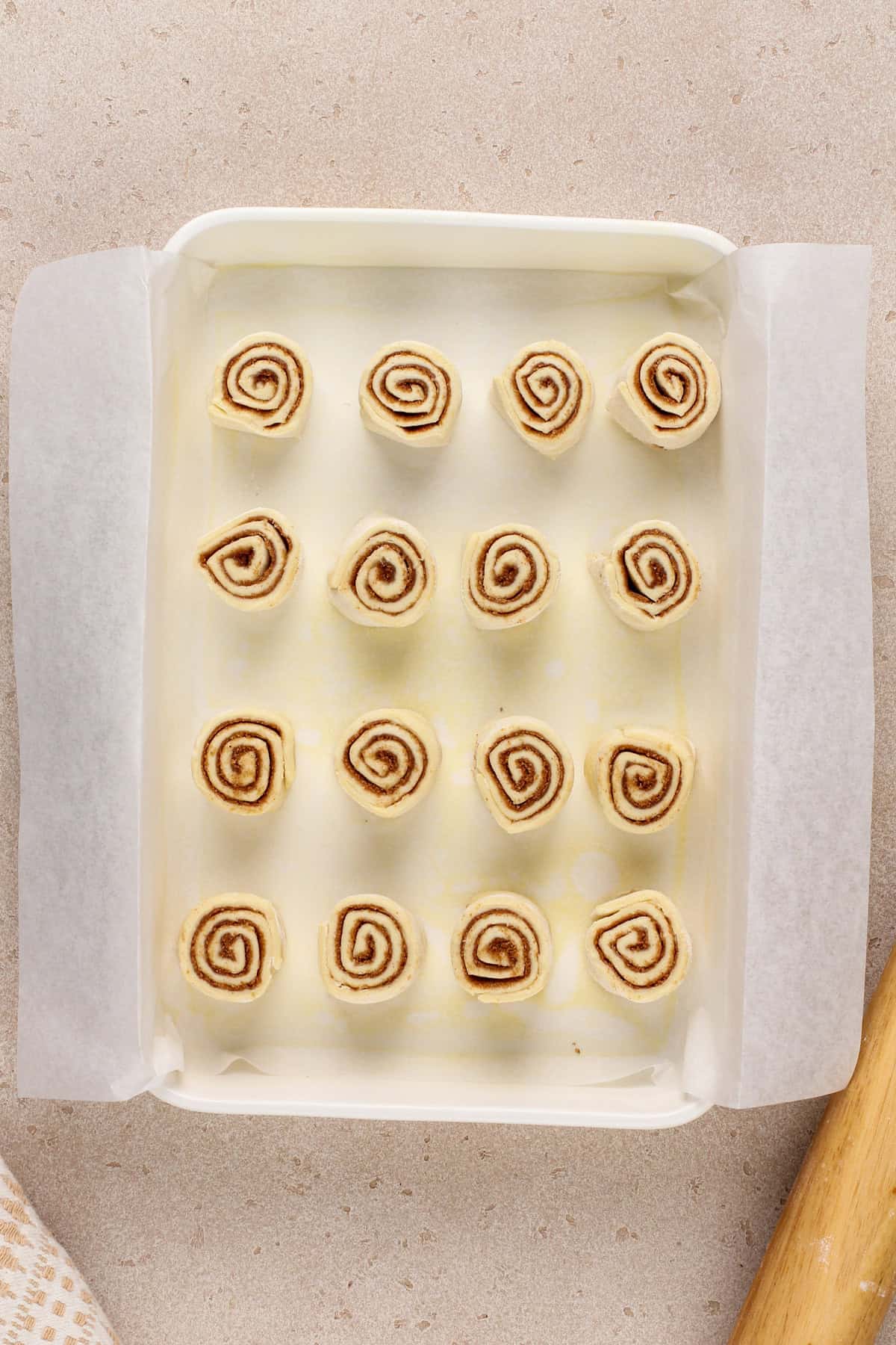 Unbaked puff pastry cinnamon rolls in a white baking pan.