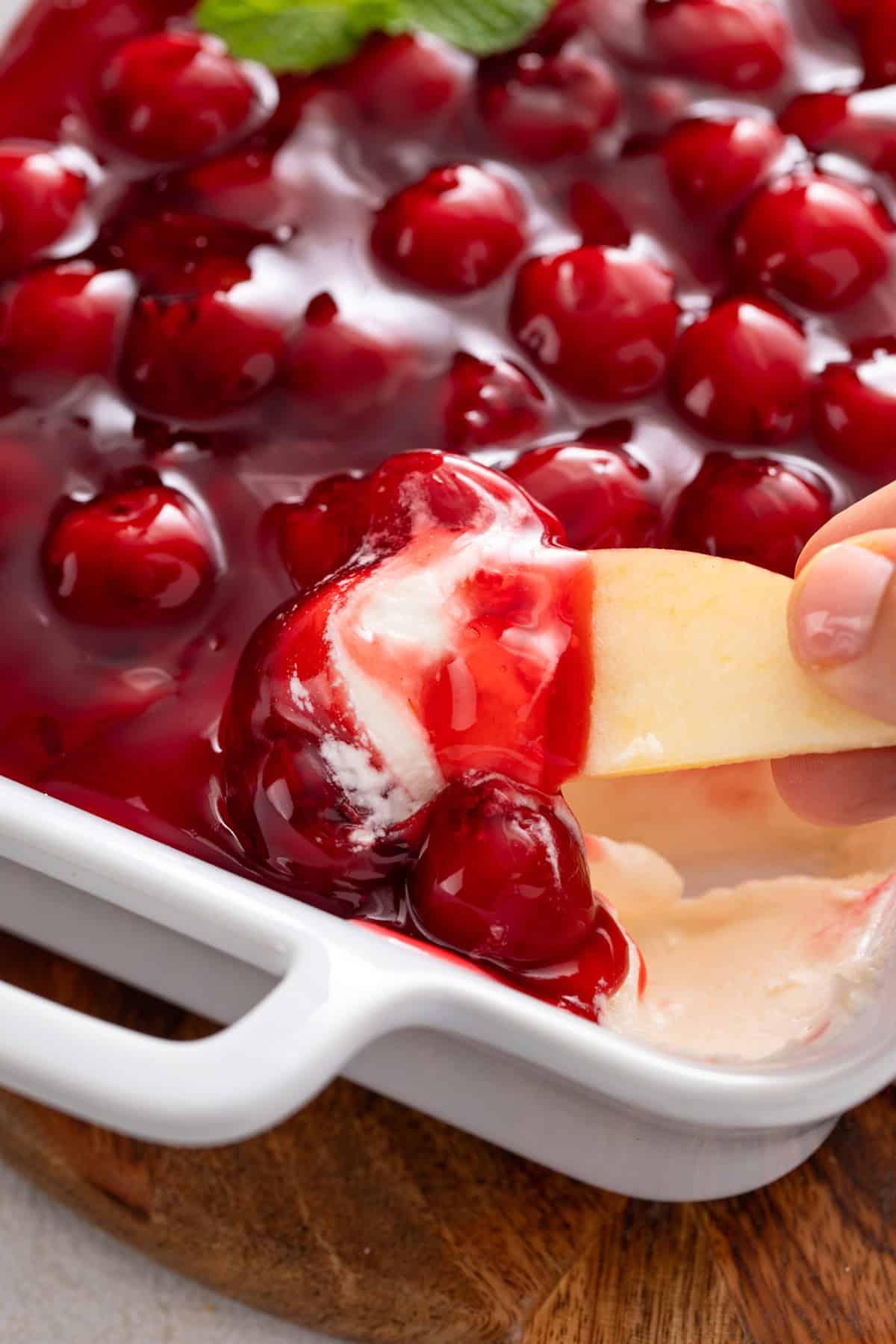 Apple slice being dipped into a dish of cherry cheesecake dip.