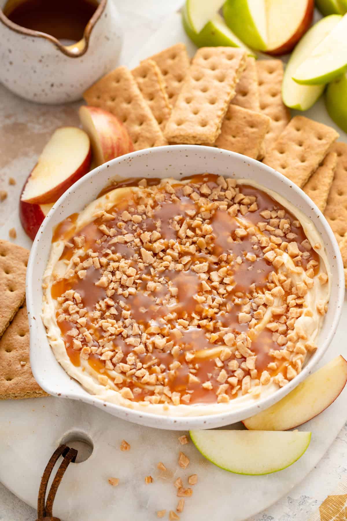 Bowl of cream cheese caramel apple dip on a platter surrounded by graham crackers and apples.