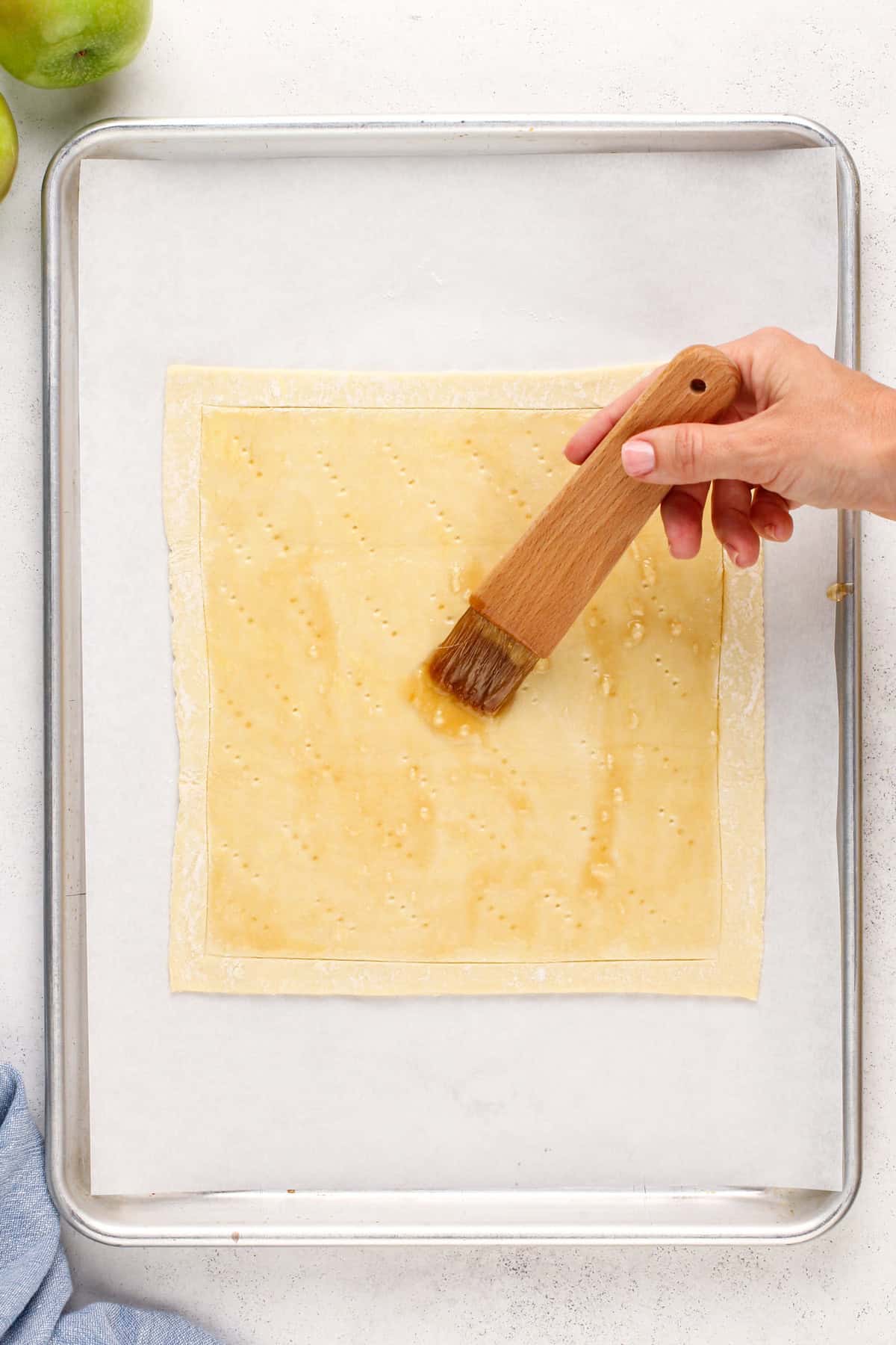 Scored sheet of puff pastry being brushed with melted apricot glaze.