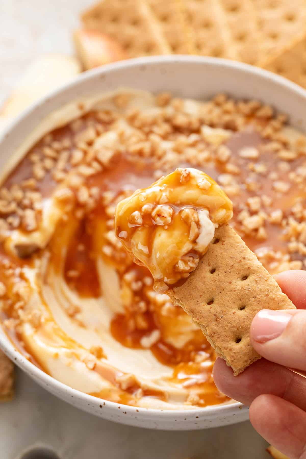 Hand holding up a piece of graham cracker with cream cheese caramel apple dip on it.