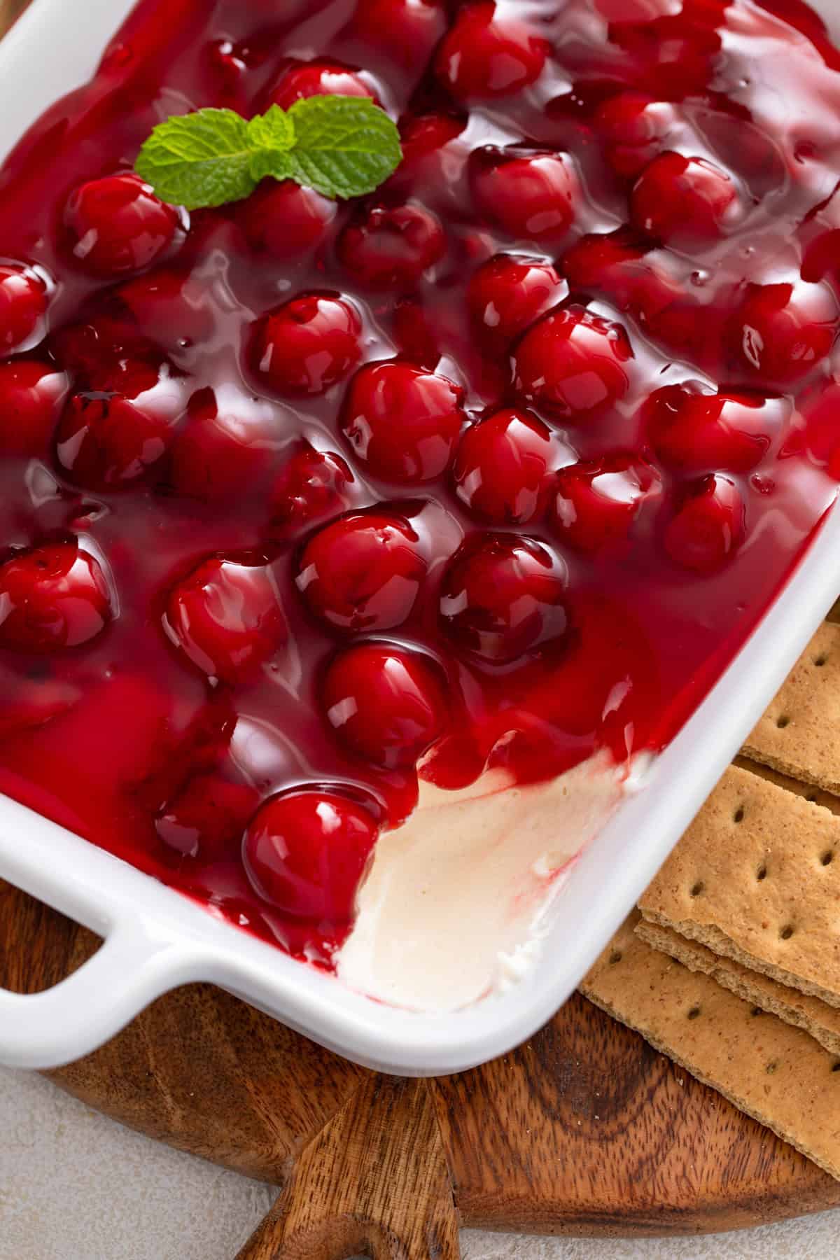 Serving dish of cherry cheesecake dip with some of the dip removed from the corner.