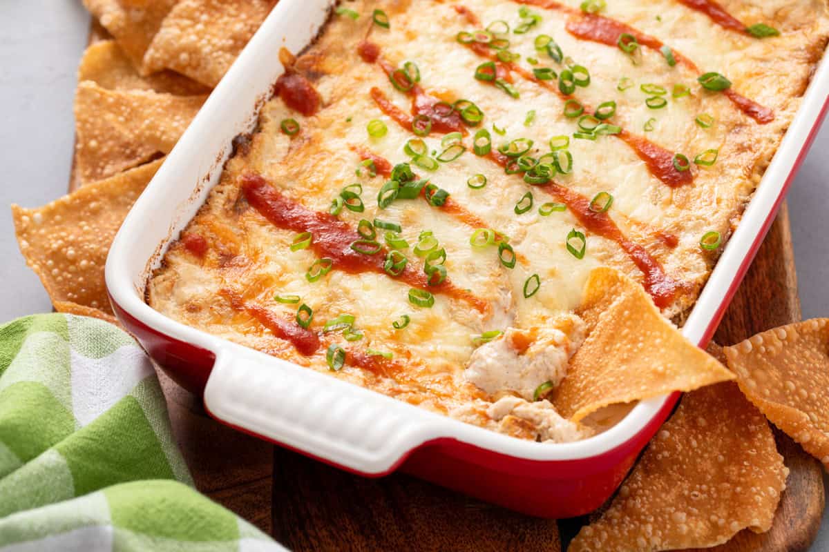 Baking dish of crab rangoon dip with a wonton chip in the corner.