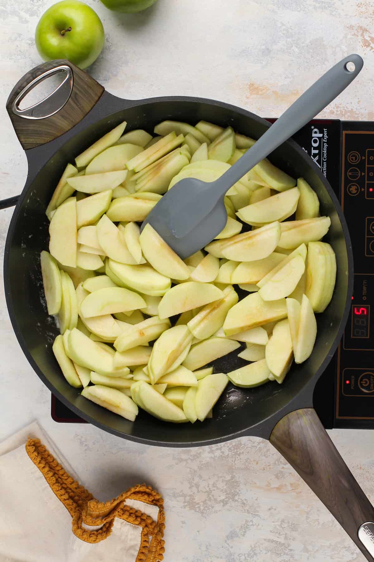 Sliced apples being cooked in a black skillet.