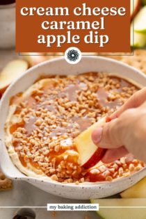 Apple slice being dipped into a bowl of cream cheese caramel apple dip. Text overlay includes recipe name.