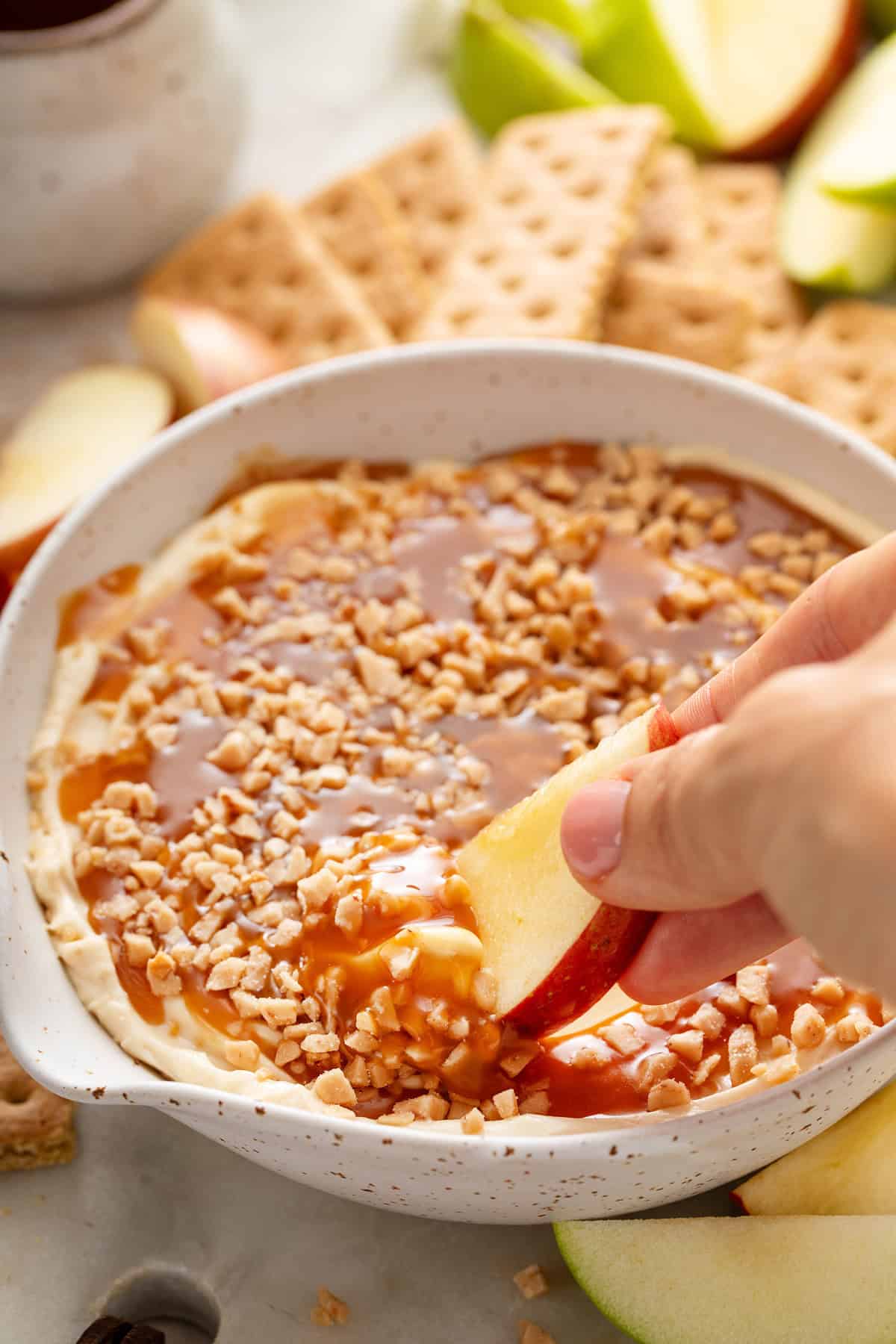 Apple slice being dipped into a bowl of cream cheese caramel apple dip.