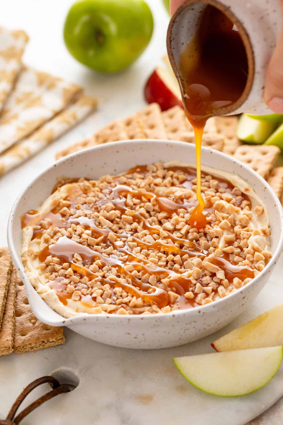 Caramel sauce being drizzled over the top of cream cheese caramel apple dip in a bowl.