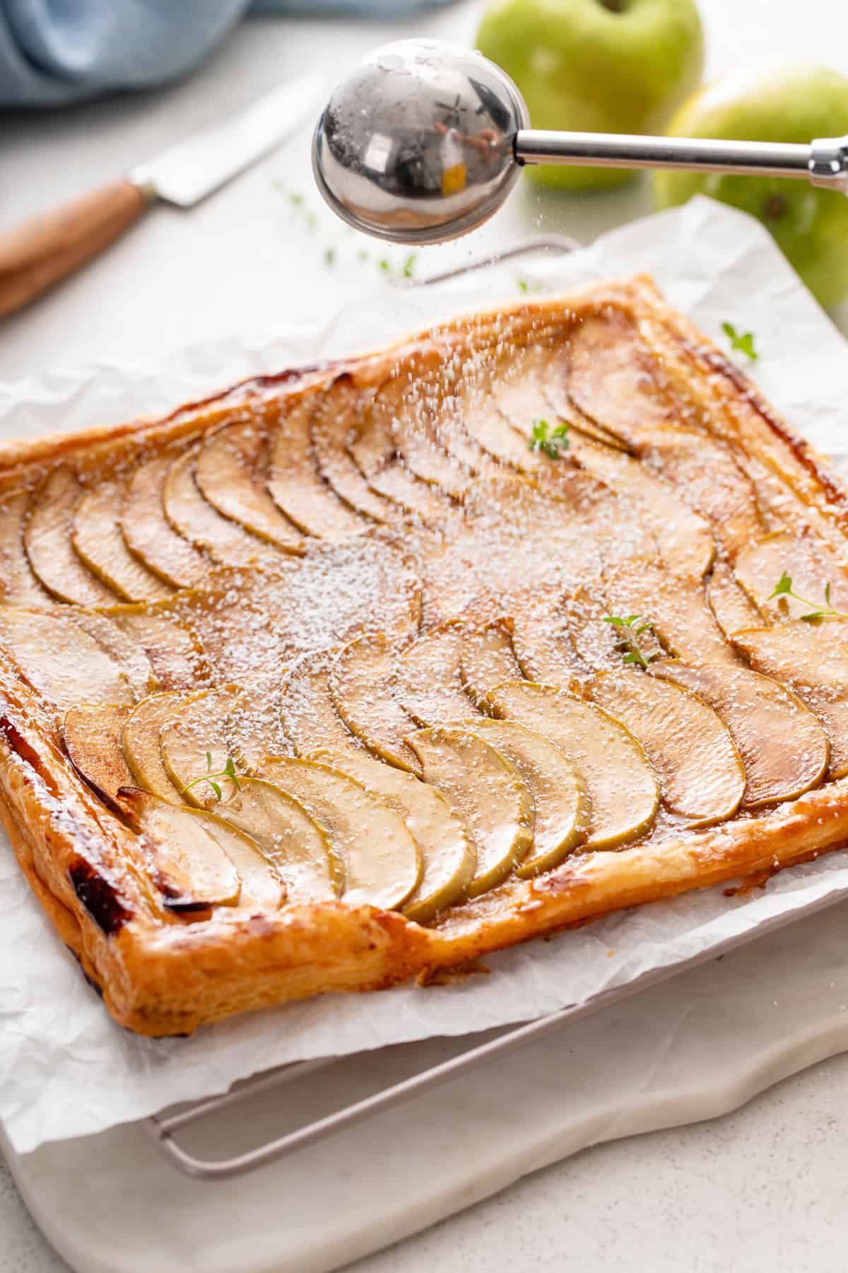 Dusting powdered sugar on top of puff pastry apple tart.