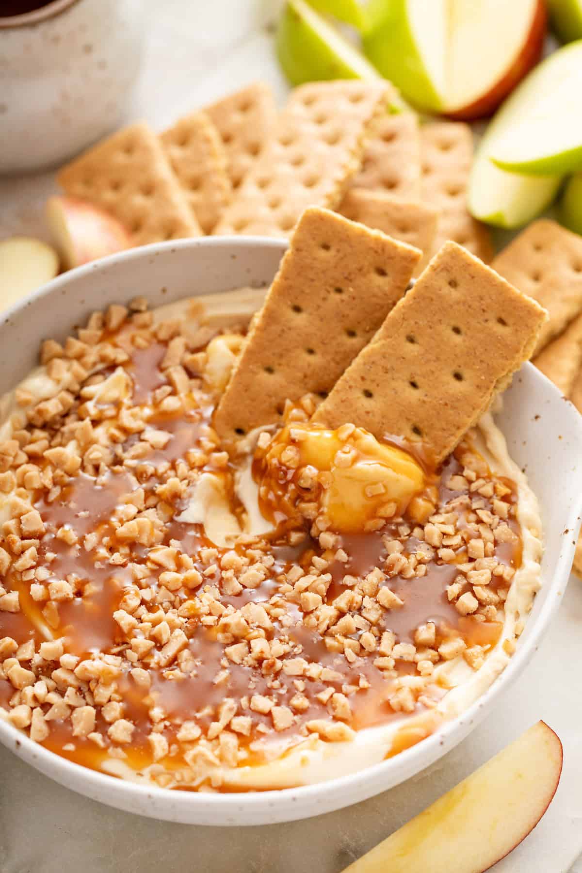 Graham crackers in a bowl of cream cheese caramel apple dip.